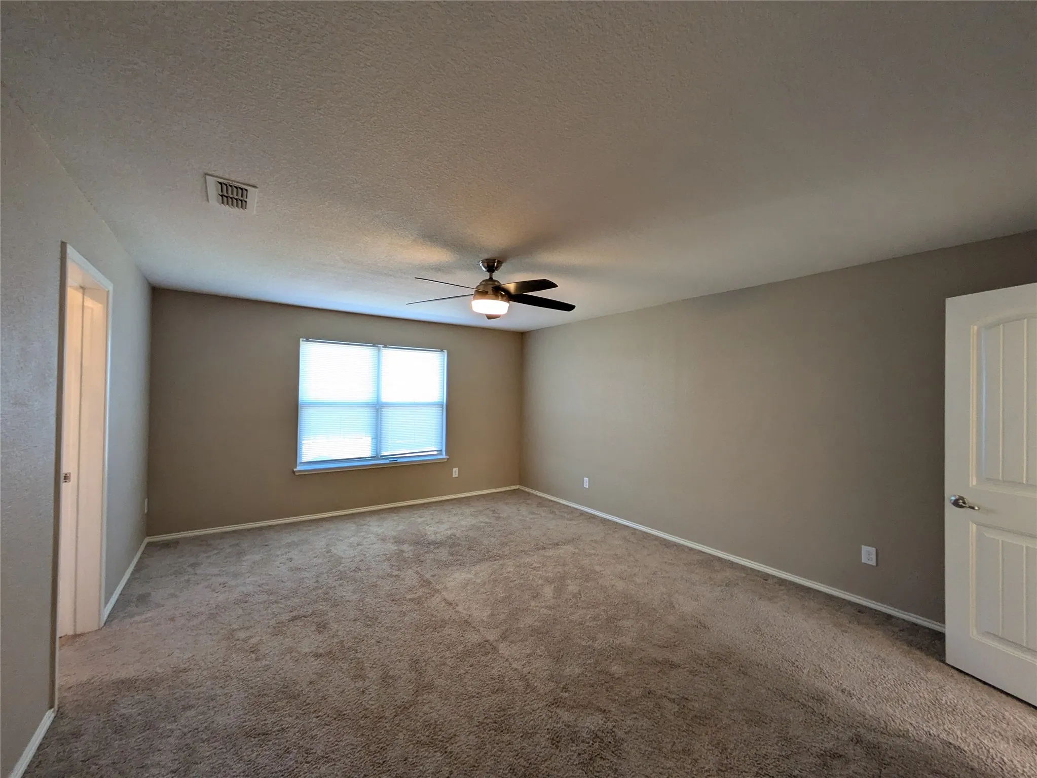 Spare room featuring ceiling fan, a textured ceiling, and light carpet
