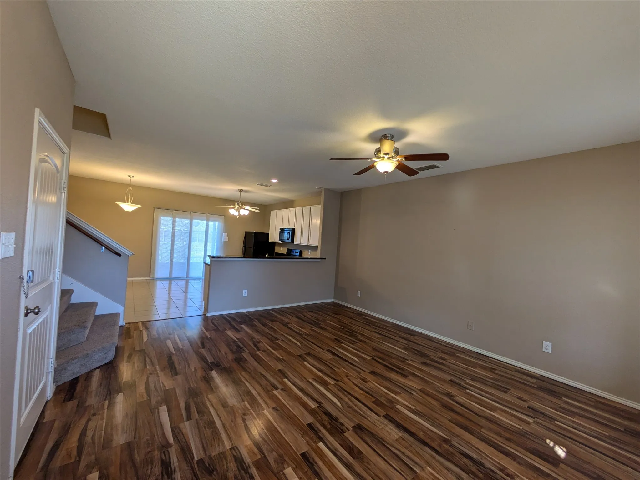 Unfurnished living room with ceiling fan with notable chandelier and dark hardwood / wood-style flooring