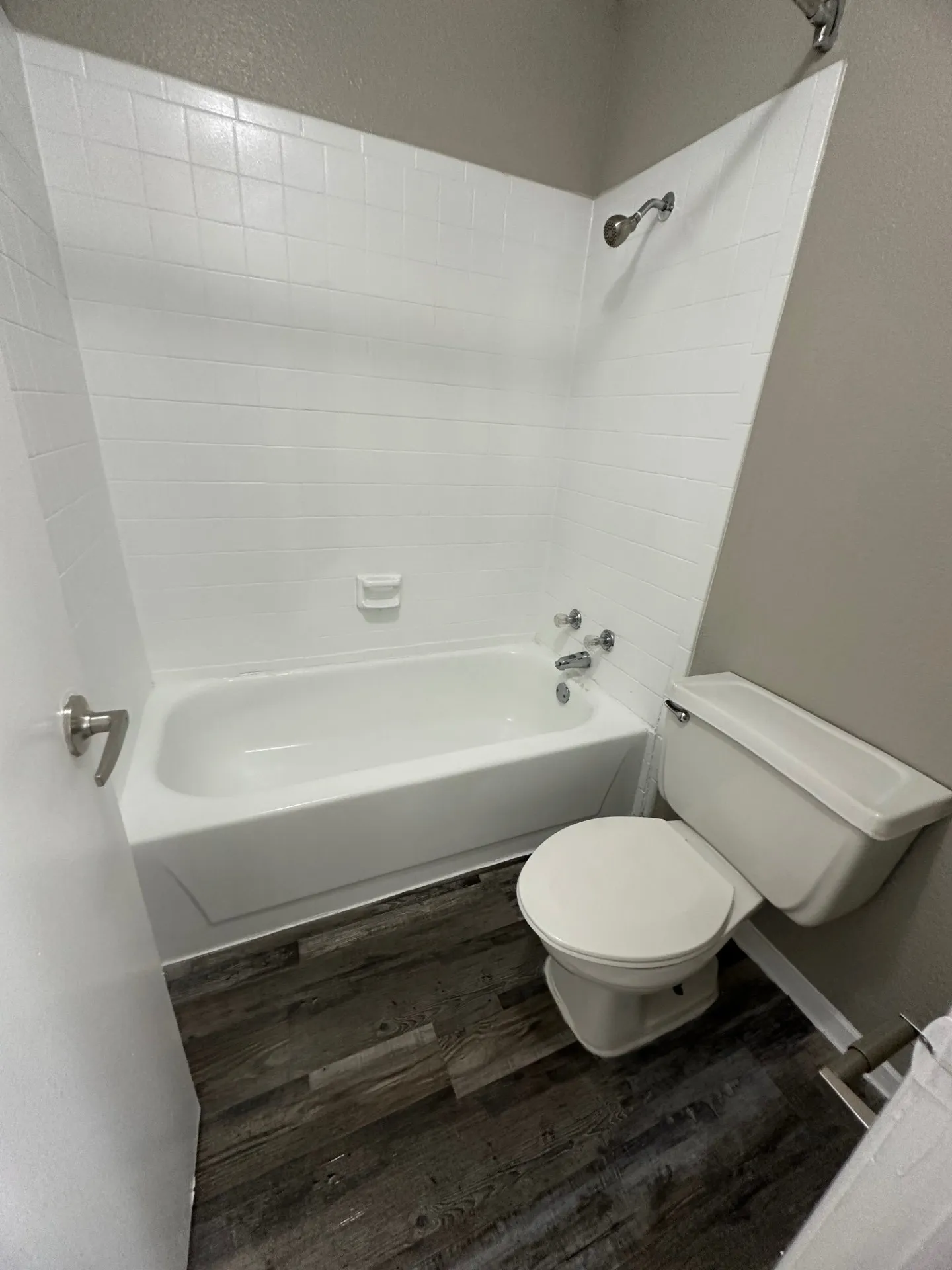 Bathroom featuring a white tub and shower combination with white subway tile surround, chrome fixtures, and wood-finish flooring