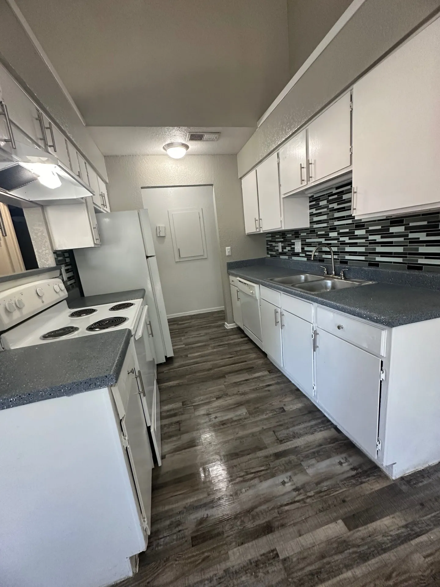 Kitchen featuring wood-finish flooring, white cabinetry, dark speckled countertops, a mosaic tile backsplash, and a double basin stainless steel sink