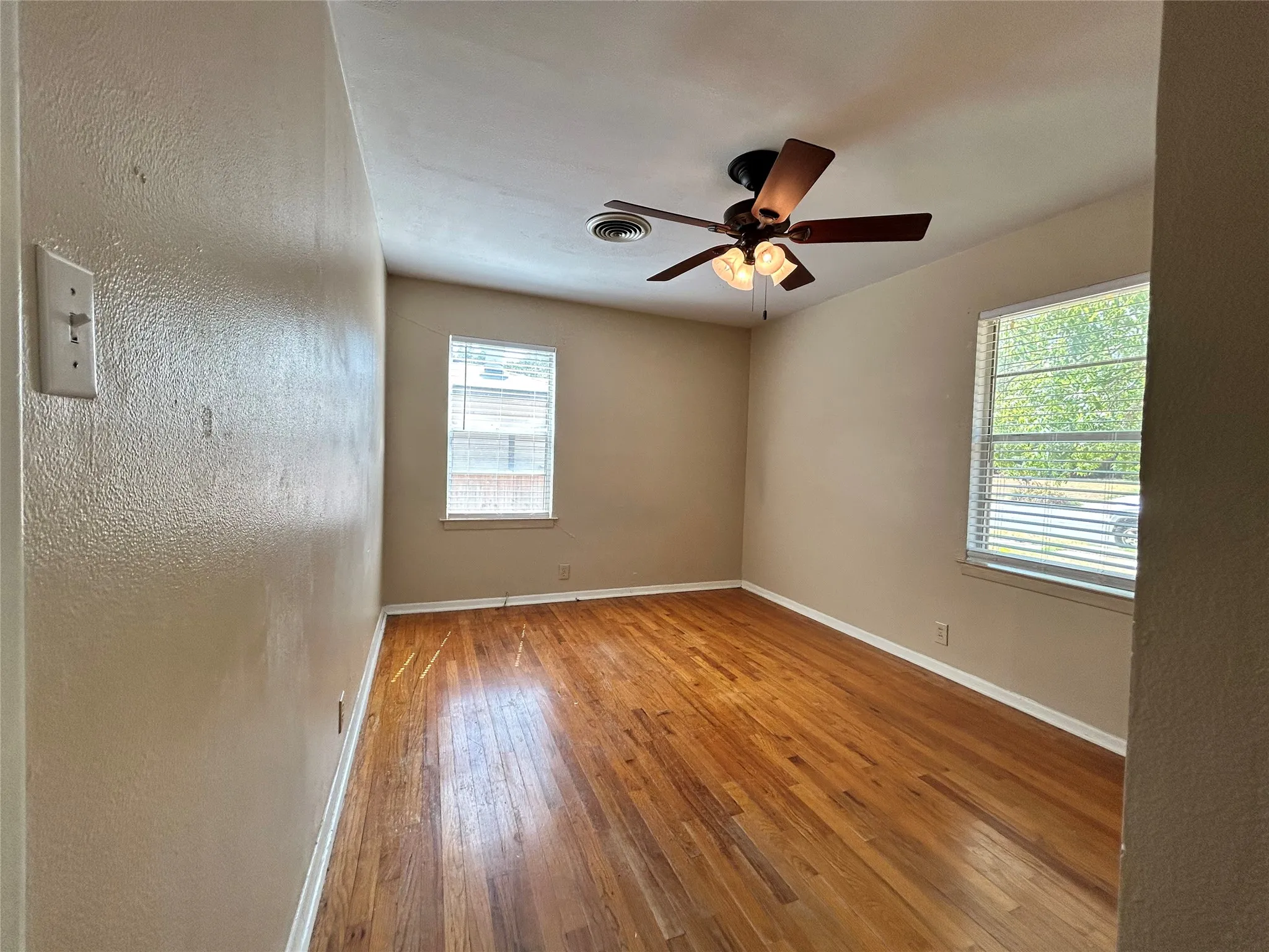 Wood-finish flooring, two windows with blinds, and a ceiling fan with integrated lighting