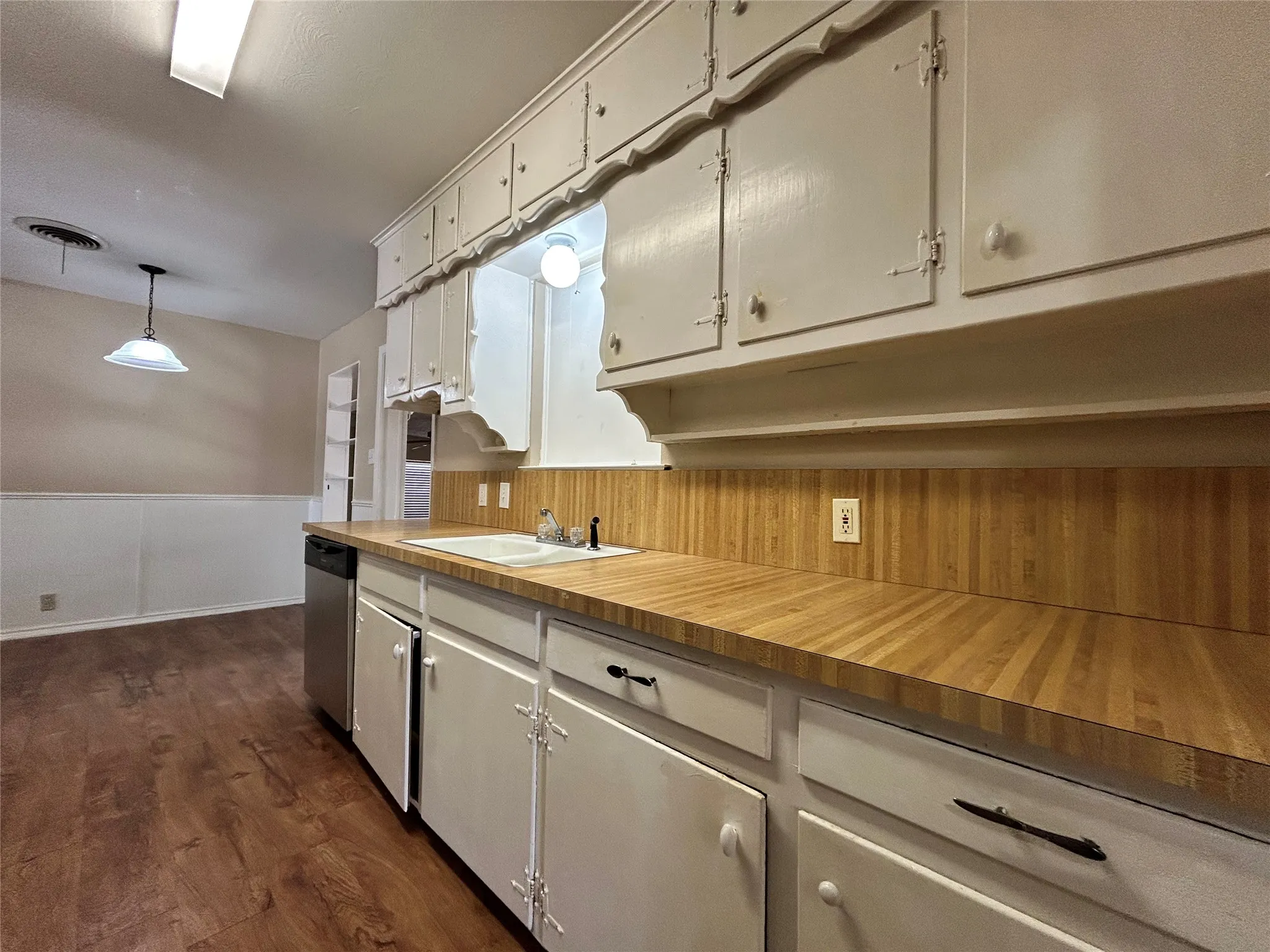 Kitchen with wood-finish countertops, white cabinetry, and stainless steel dishwasher