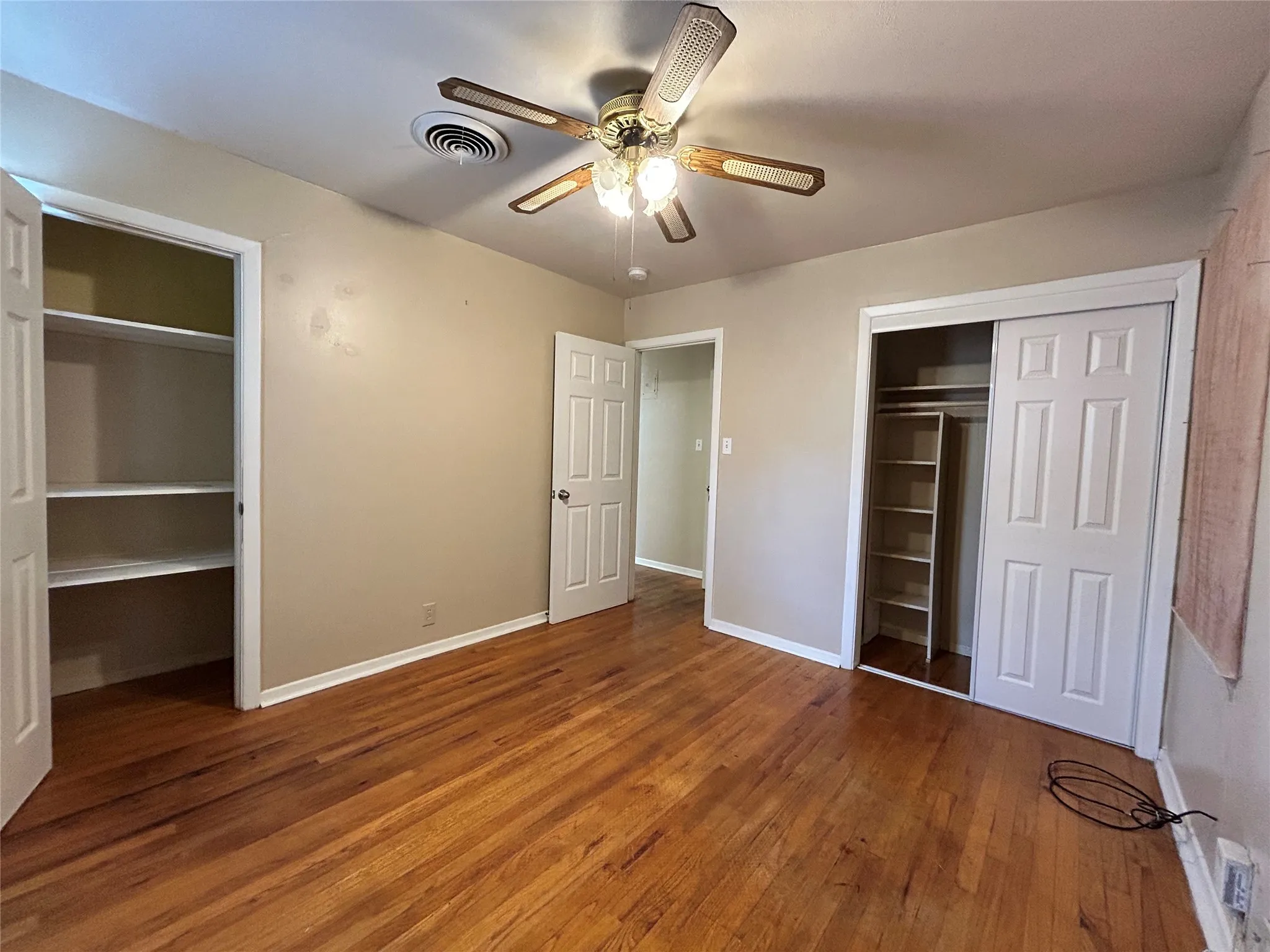 Wood-finish flooring, ceiling fan with light fixture, built-in shelving, paneled doors, and neutral wall paint