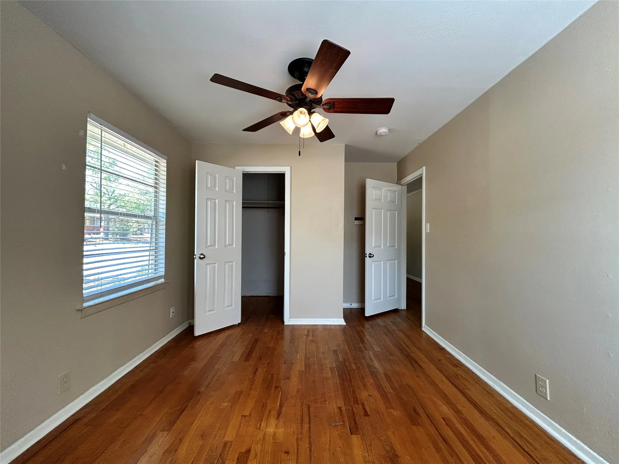 Wood-finish flooring, ceiling fan with integrated lighting, window with blinds, and paneled doors