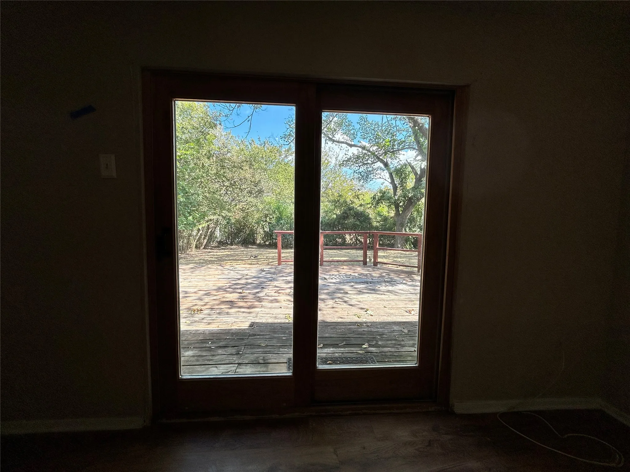 Double-pane glass patio doors opening to an exterior wood-finish deck with railing, surrounded by mature trees
