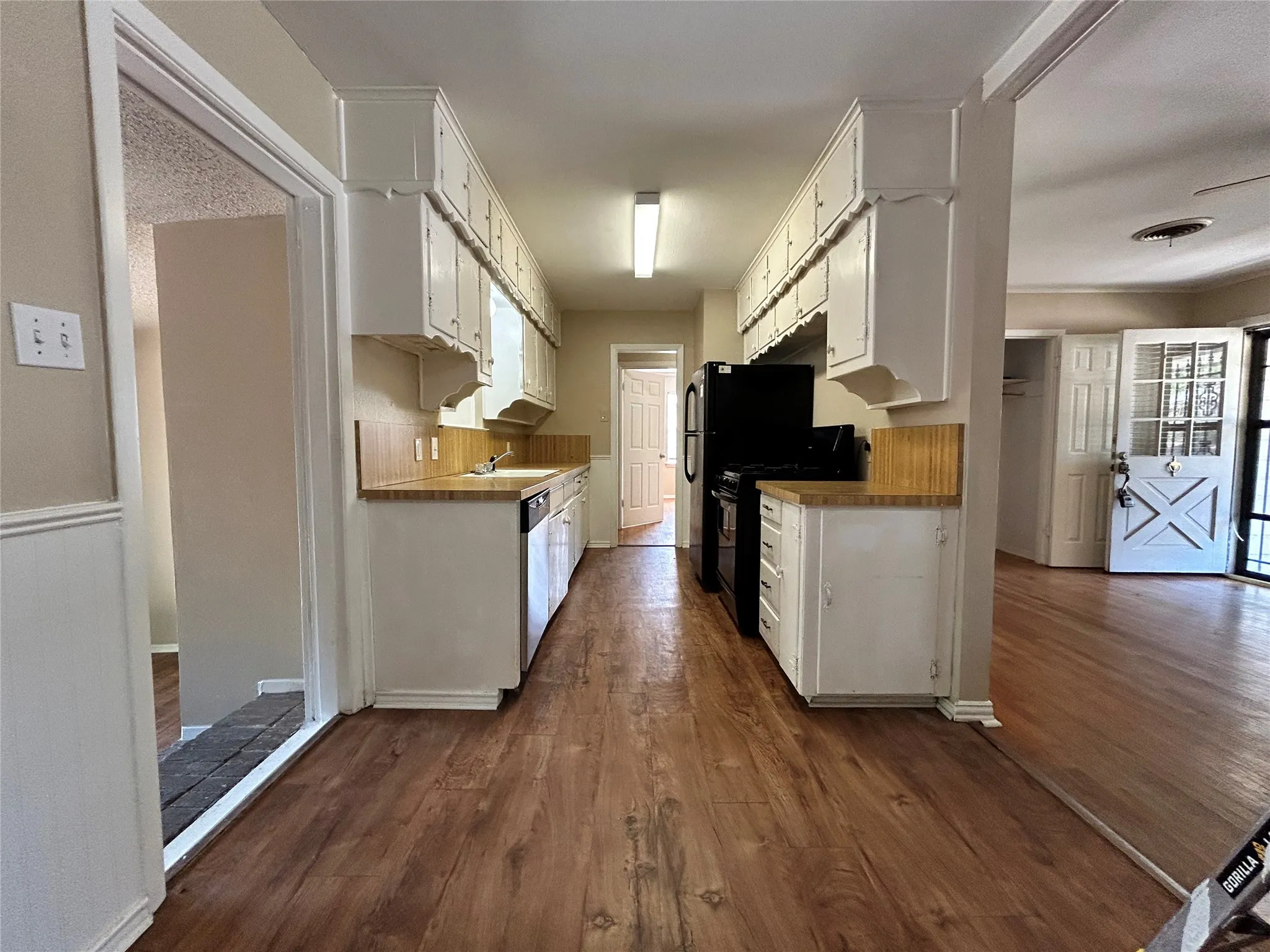Galley kitchen with wood-finish flooring, white cabinetry, integrated dishwasher, and wood-finish countertops