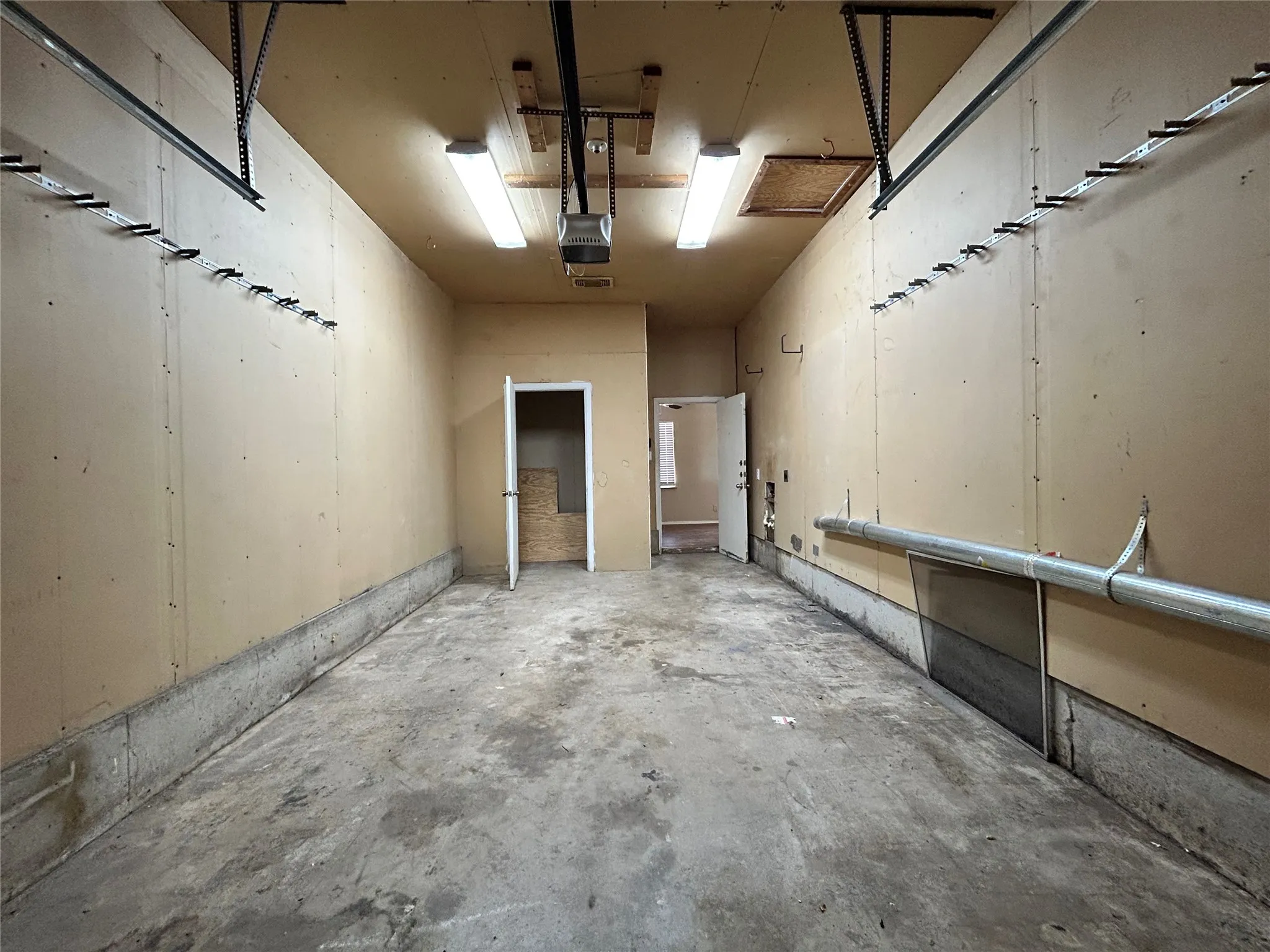 Concrete floor, exposed wood-finish walls, overhead lighting, garage door track system, interior access door