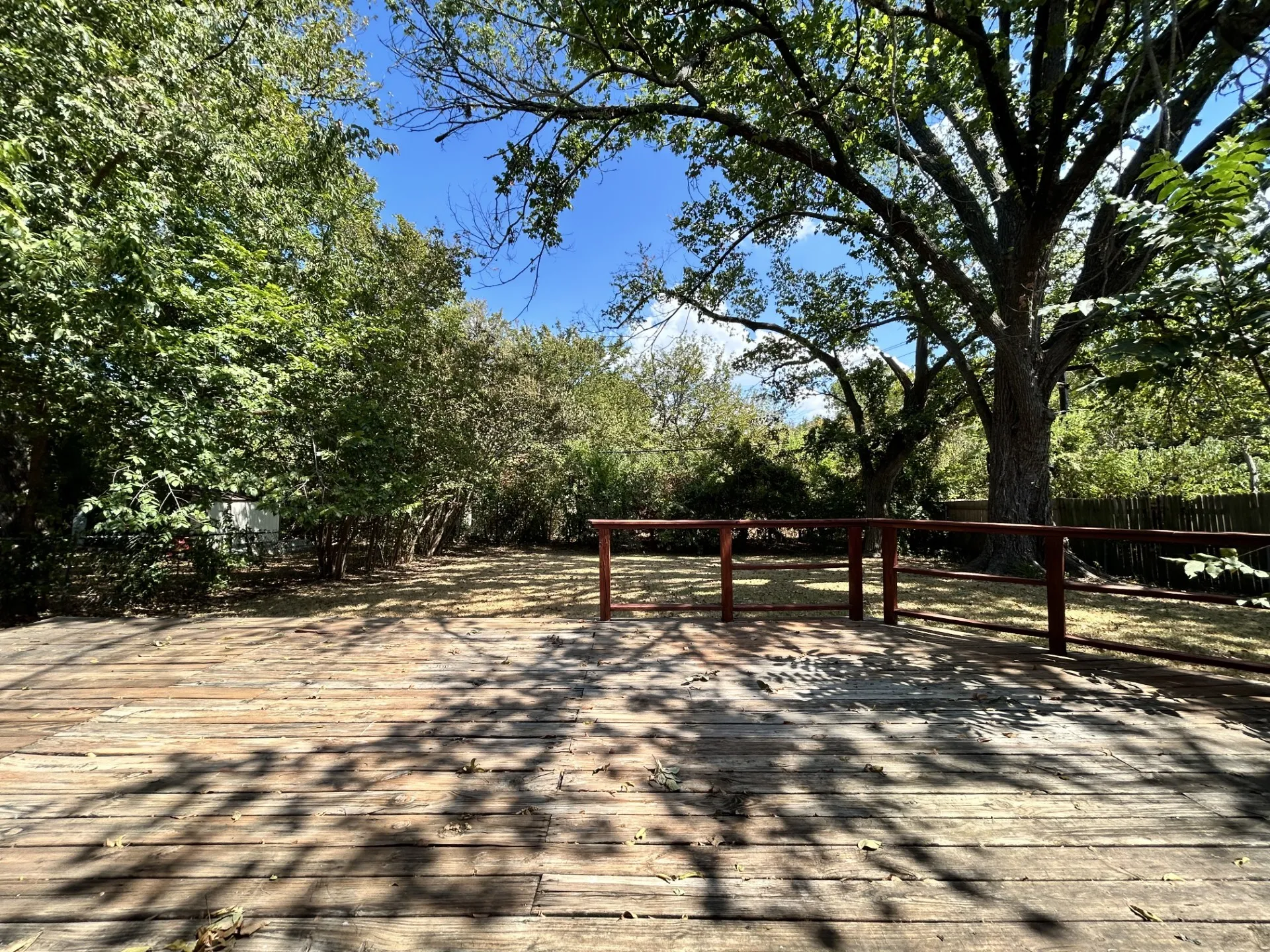 Expansive wooden deck with a protective railing, surrounded by mature trees providing natural shading