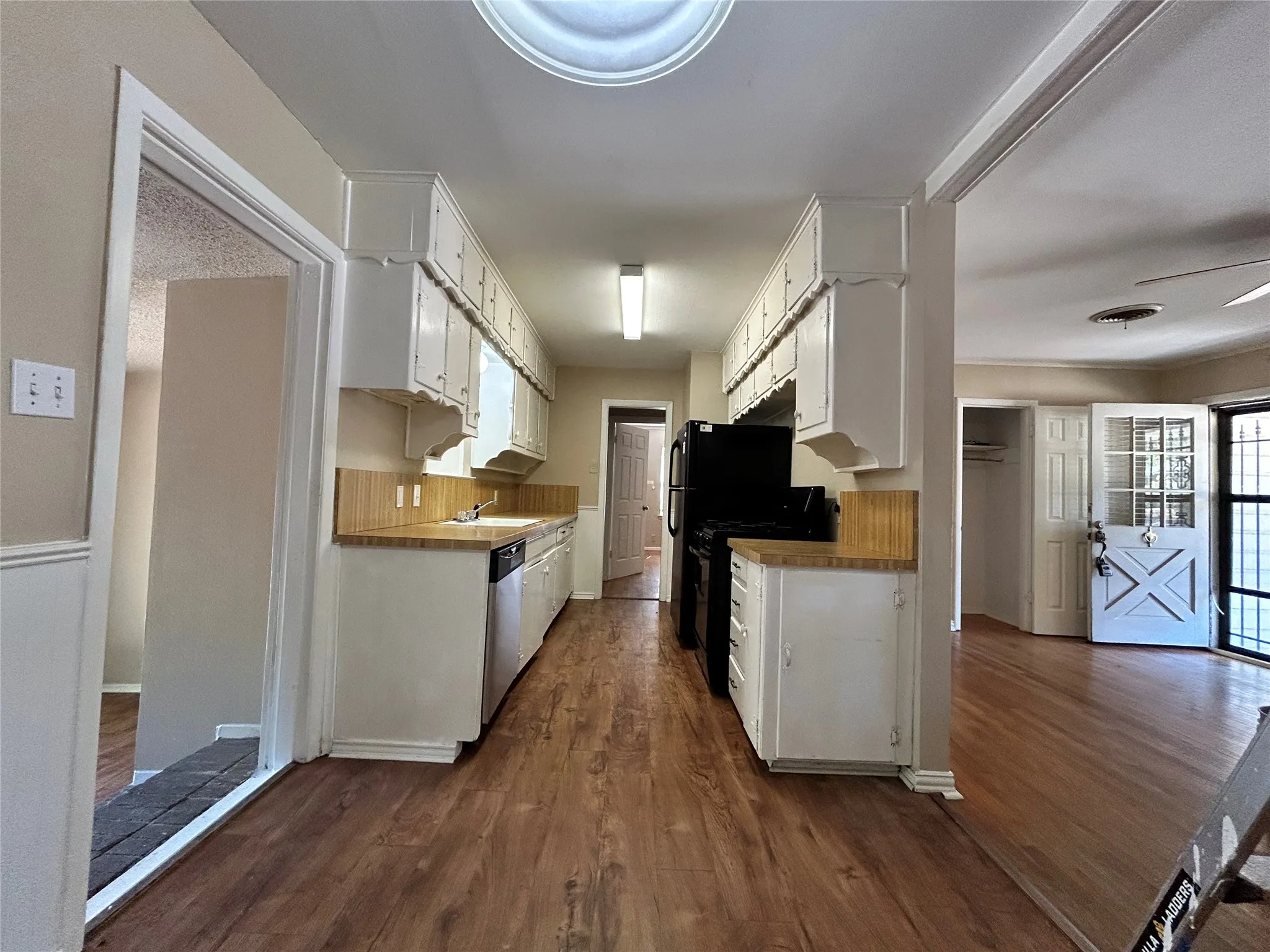 Galley kitchen with wood-finish flooring, white cabinetry, integrated dishwasher, and black appliances