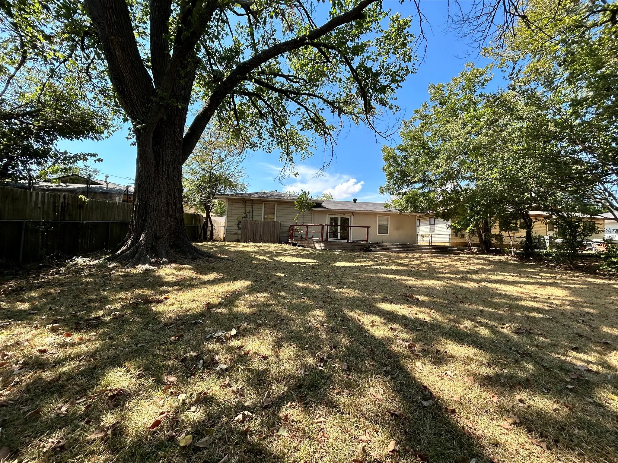 Expansive rear yard with mature trees, a wood deck, and a privacy fence