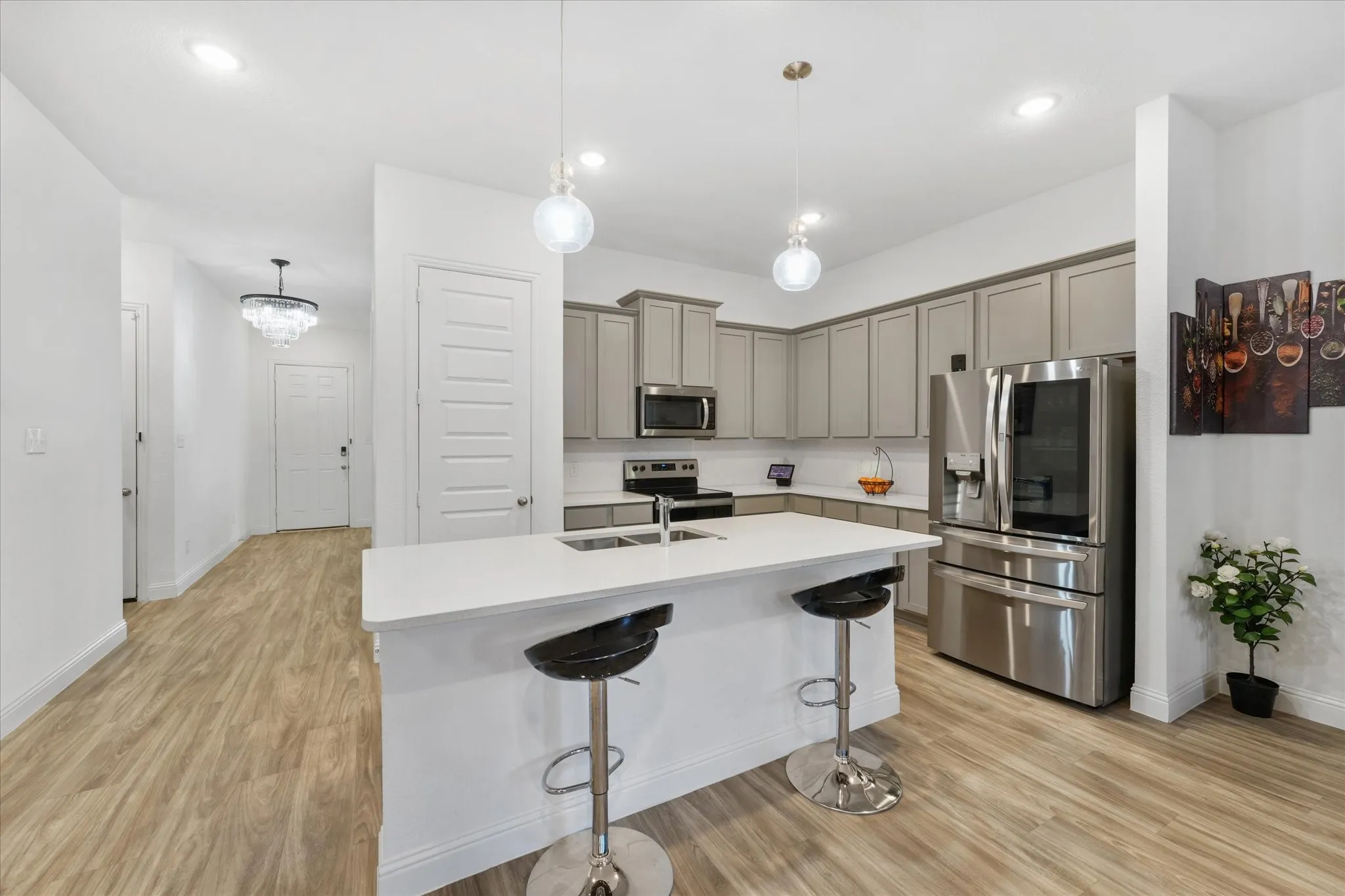 Modern kitchen featuring light gray cabinetry, stainless steel appliances, a white island with pendant lighting, and wood-finish flooring