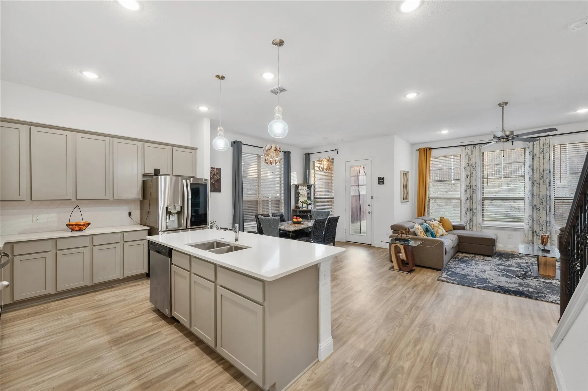 Open-concept living area featuring wood-finish flooring throughout, a modern kitchen island with an undermount sink, recessed lighting, a ceiling fan, and multiple windows