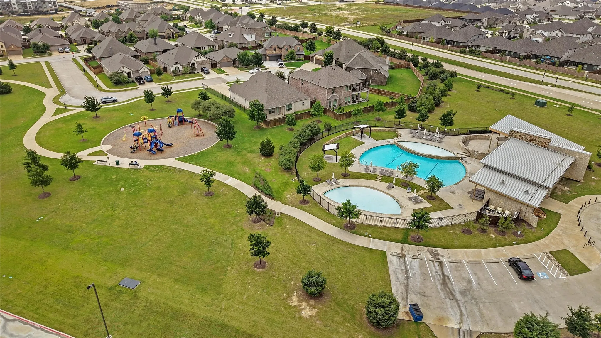 Community amenities featuring two swimming pools, a dedicated playground area, a clubhouse structure with a stone facade, walking paths, and expansive green spaces