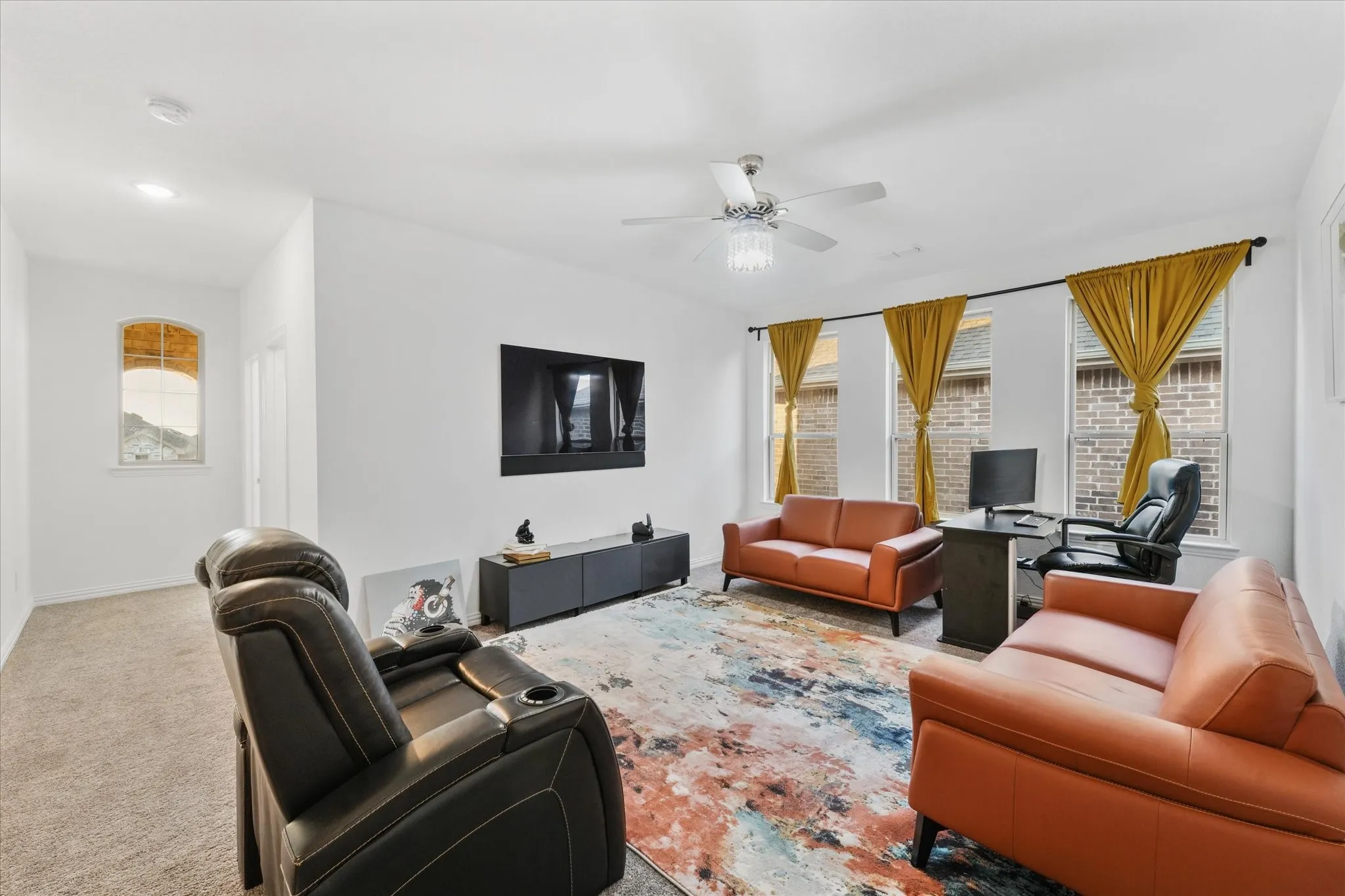 Spacious living area featuring neutral carpeting, a ceiling fan with integrated lighting, and multiple windows with upper transoms