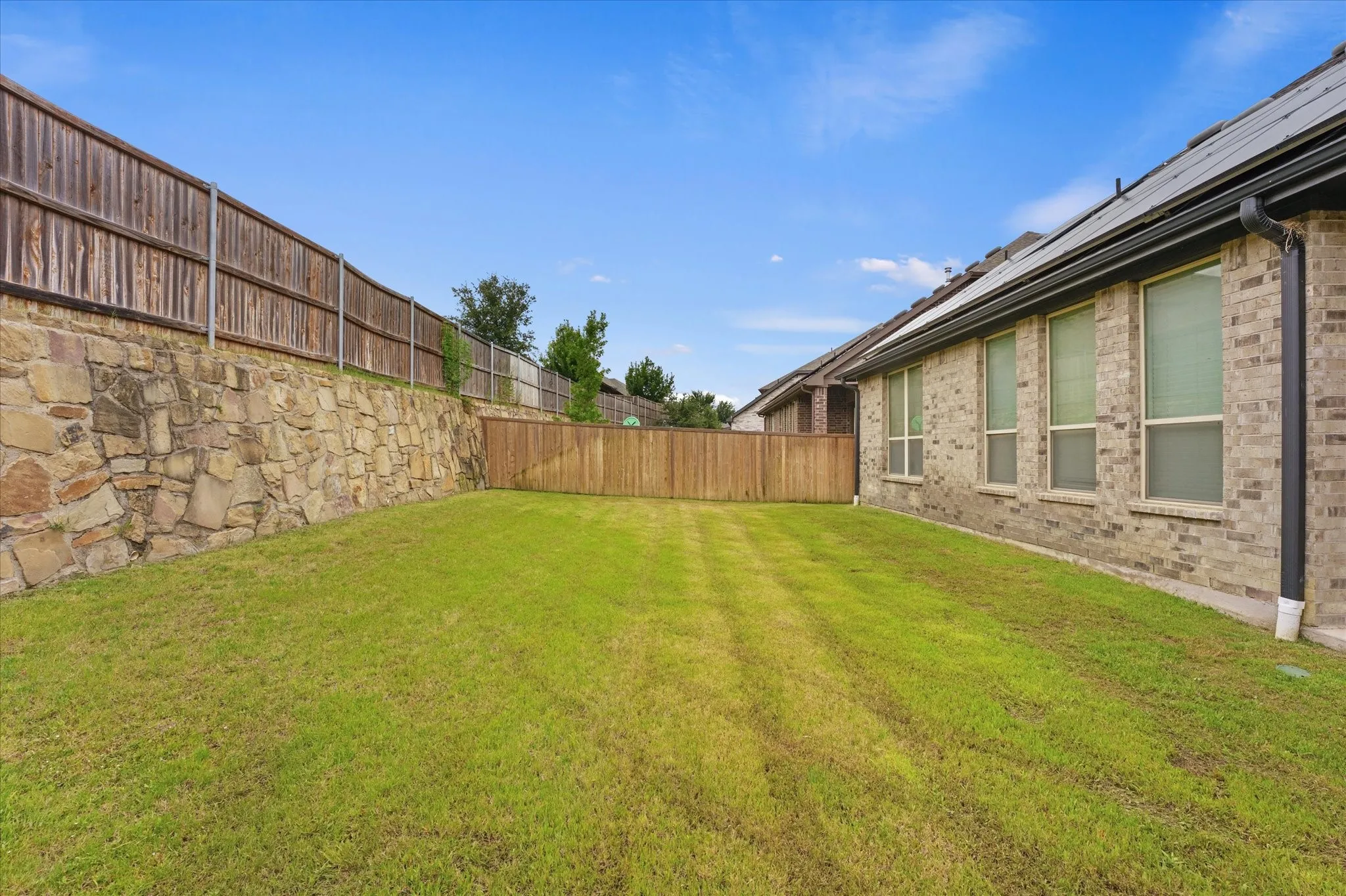 Expansive grassy yard area with a stone retaining wall and full privacy fencing