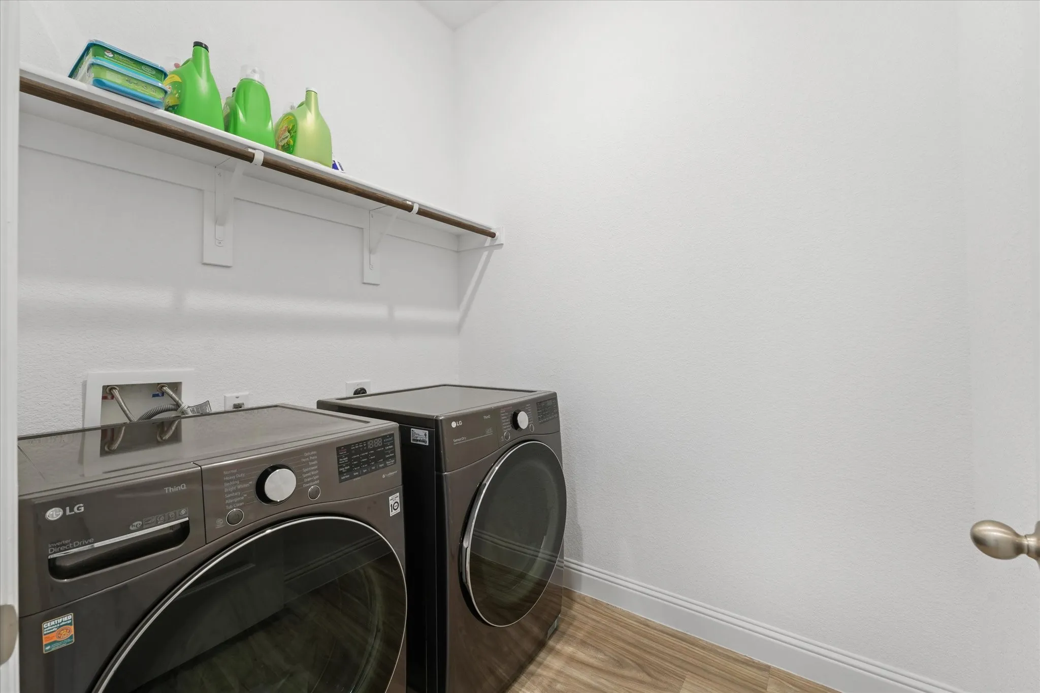 Dedicated laundry area featuring a white wall shelf with a clothing rod, wood-finish flooring, and crisp white trim