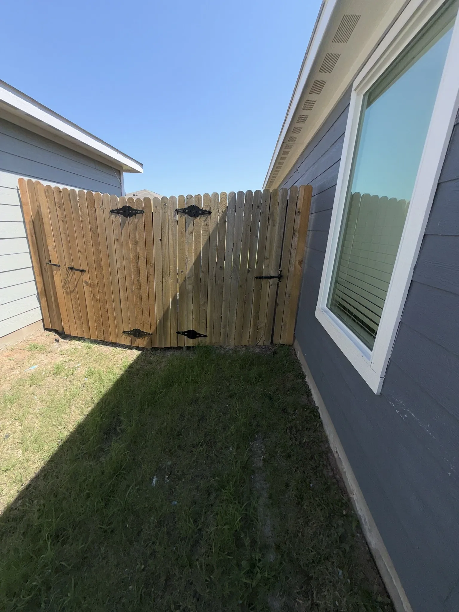 Wood privacy fence with decorative black hardware, featuring a double gate and a single gate