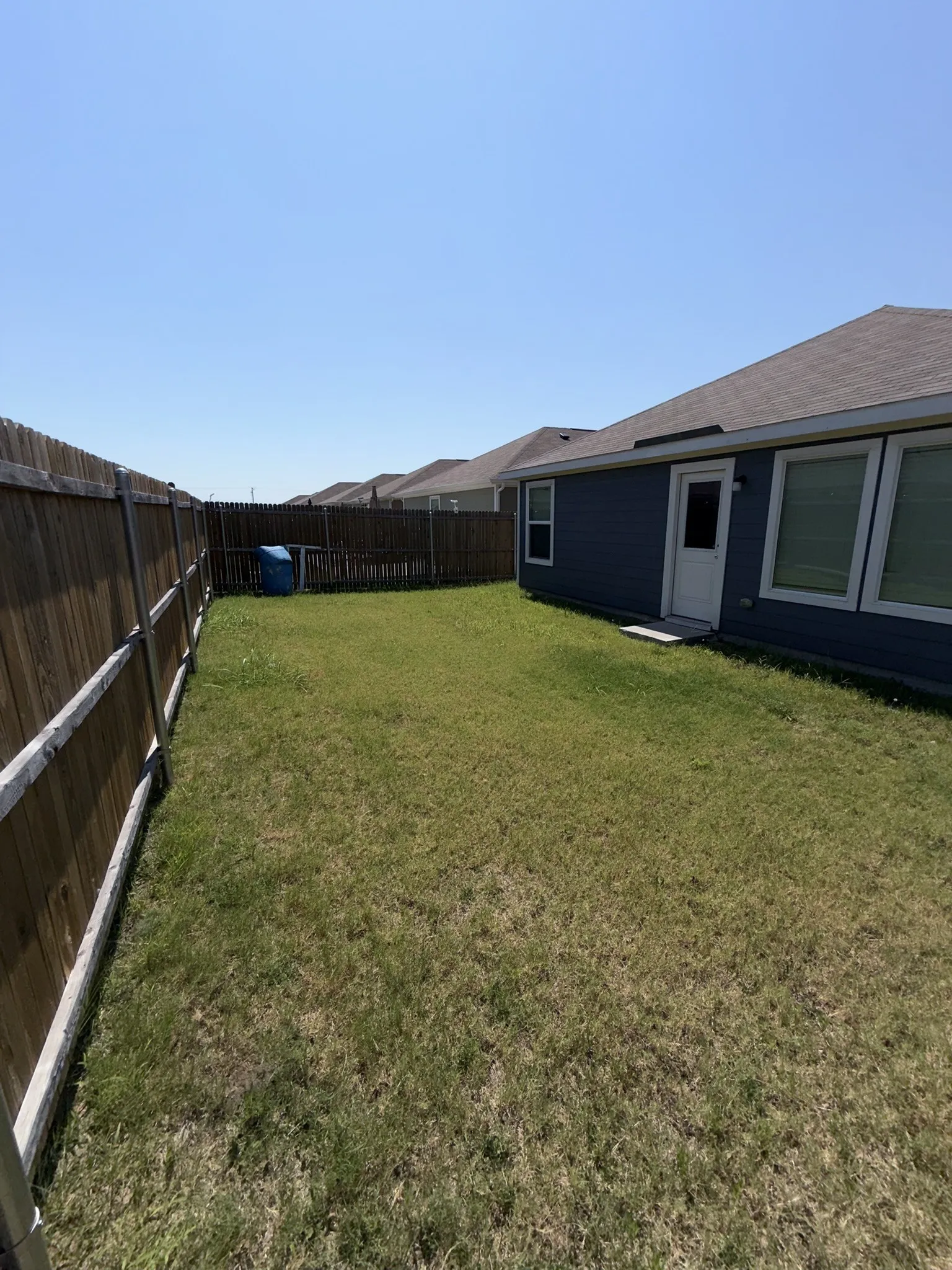 Fenced backyard with expansive lawn, featuring a side entrance door and multiple windows on the rear exterior