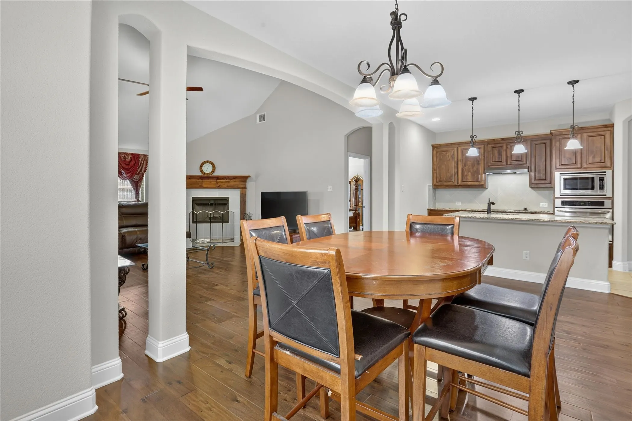 Open-concept dining area featuring wood-finish flooring, a decorative chandelier, and arched doorways