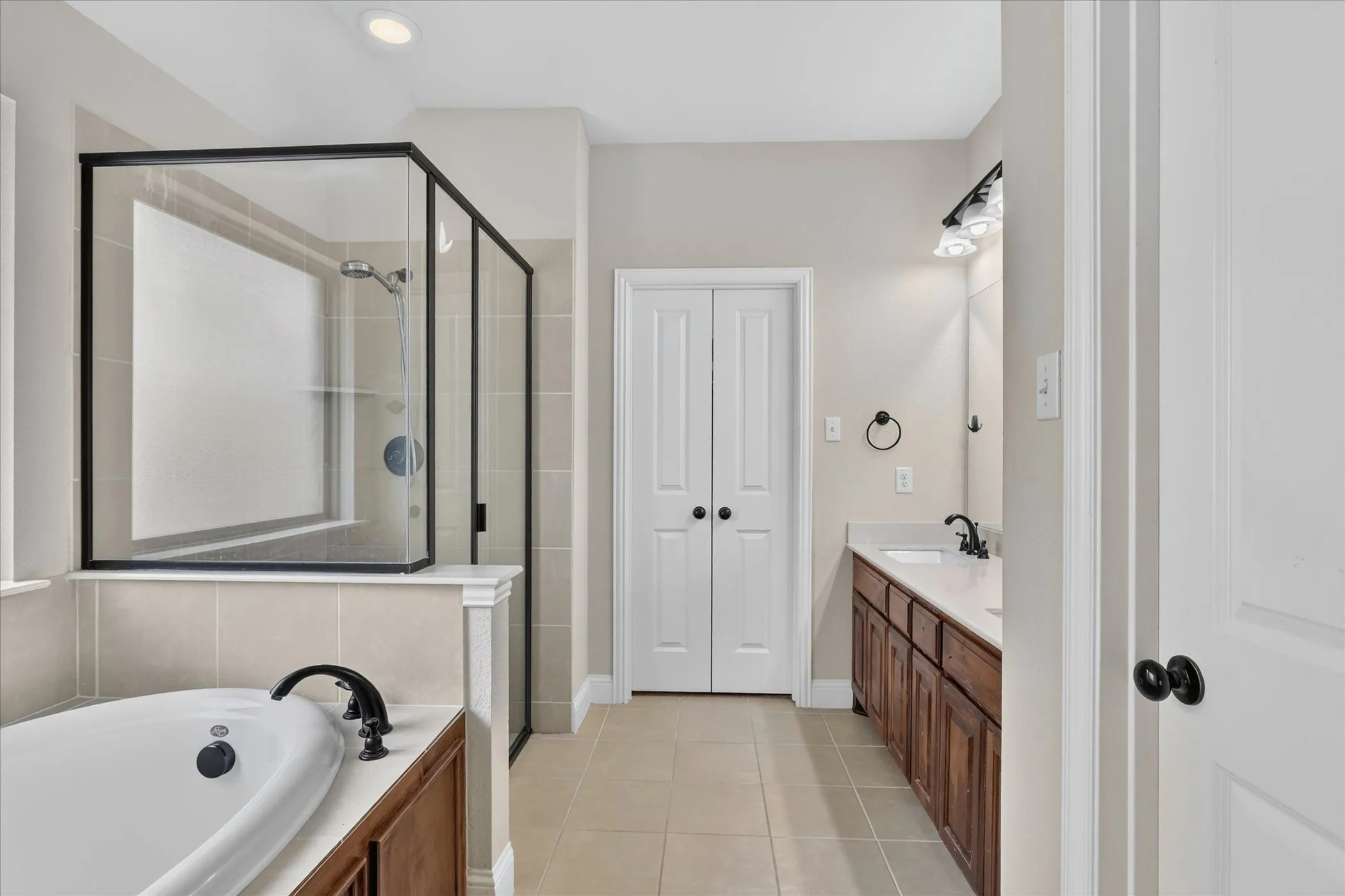 Bathroom featuring a soaking tub with black fixtures, a glass-enclosed shower with black framing, and a dual-sink vanity with dark wood cabinetry and white countertops