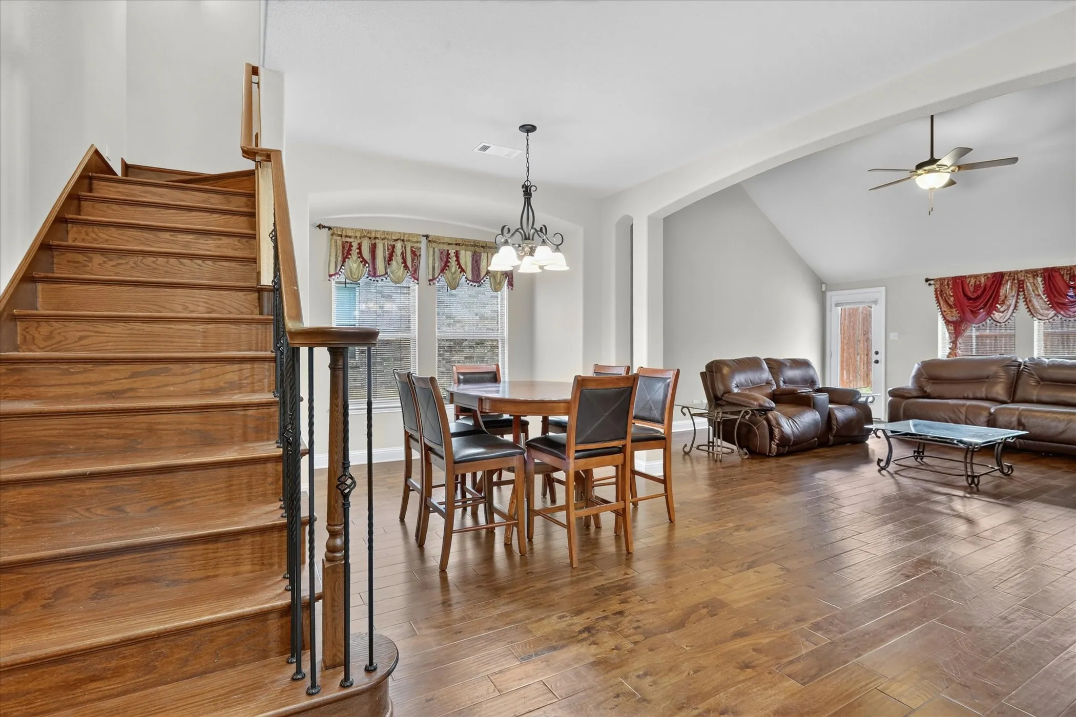 Wood-finish staircase with decorative metal spindles, complemented by wood-finish flooring throughout the open-concept space