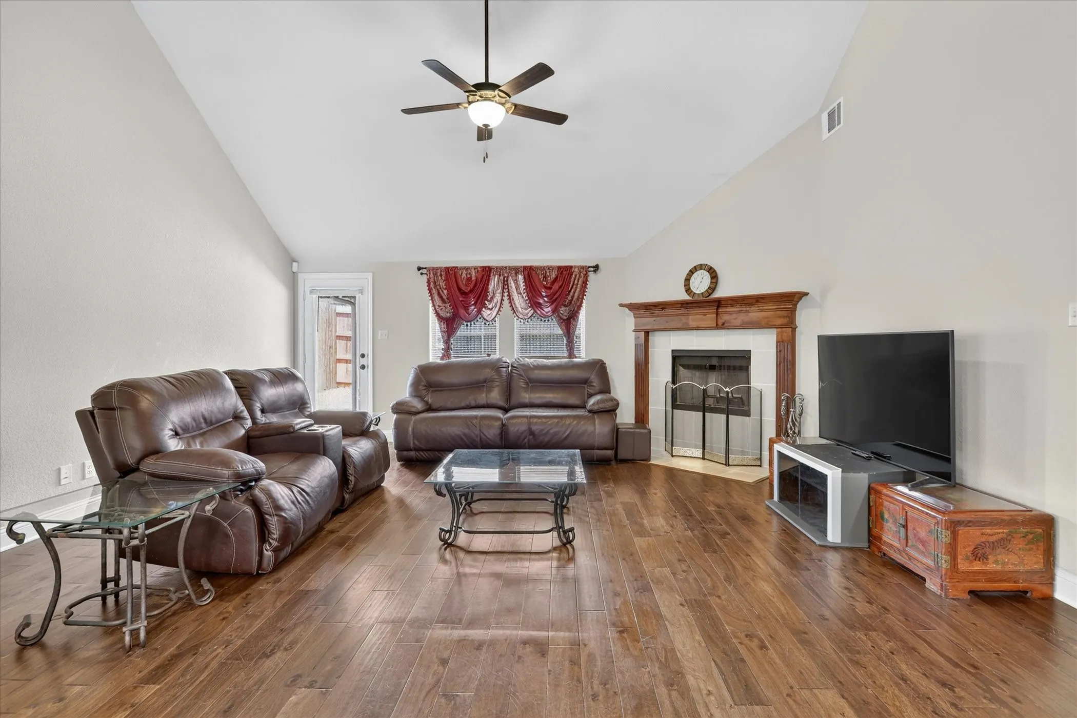 Spacious living area featuring wood-finish flooring, a vaulted ceiling, and a ceiling fan with integrated lighting