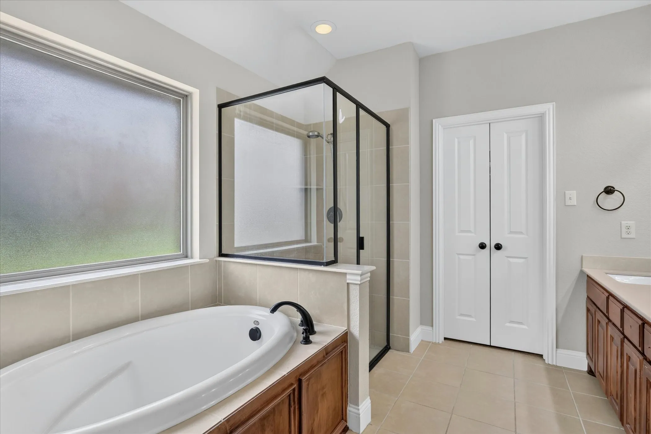 Soaking tub with oil-rubbed bronze fixtures, a frosted window, and an adjacent walk-in shower with a black-framed glass enclosure