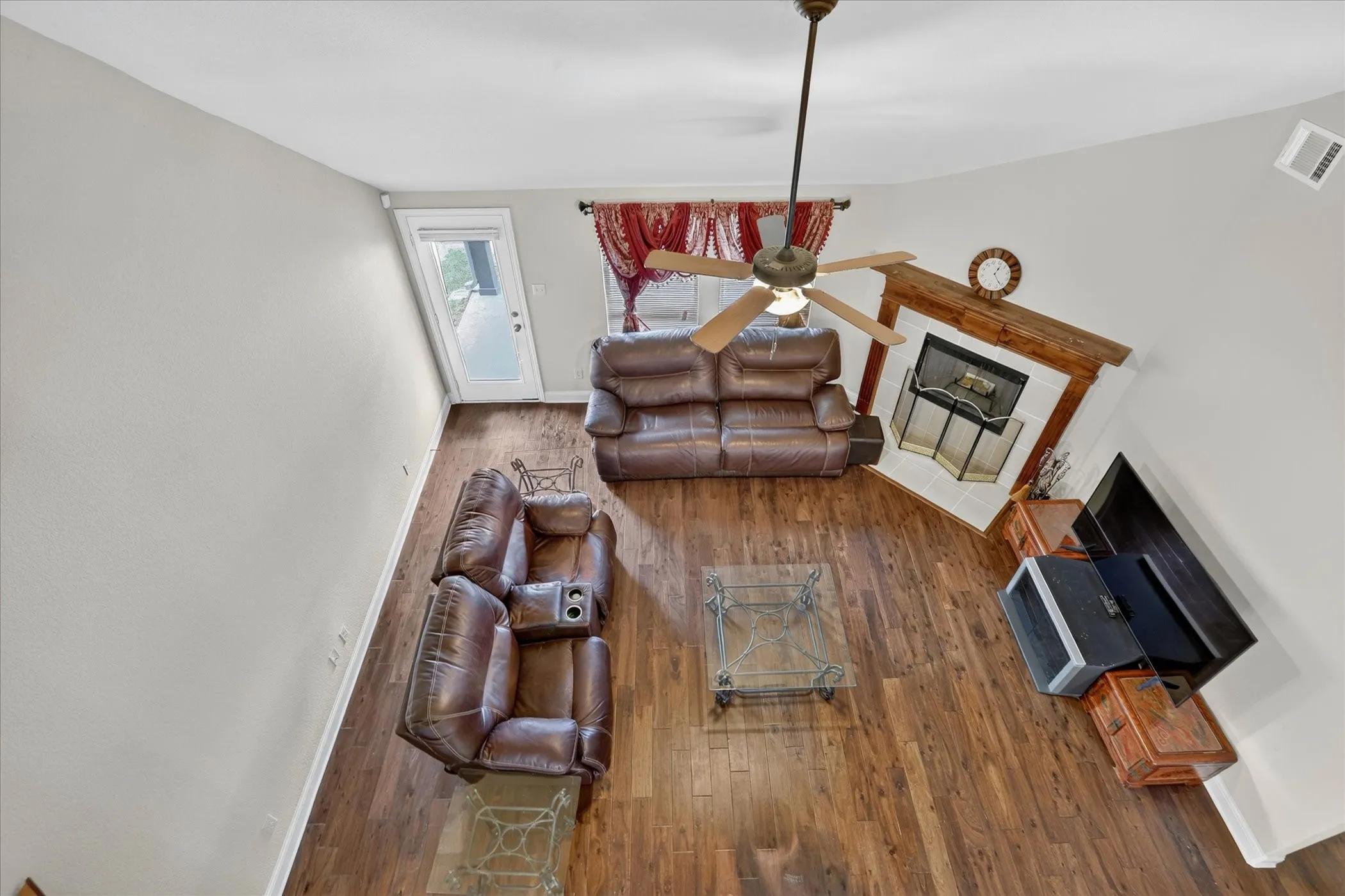 Spacious living area featuring wood-finish flooring, a corner fireplace with a wood mantle, and a ceiling fan