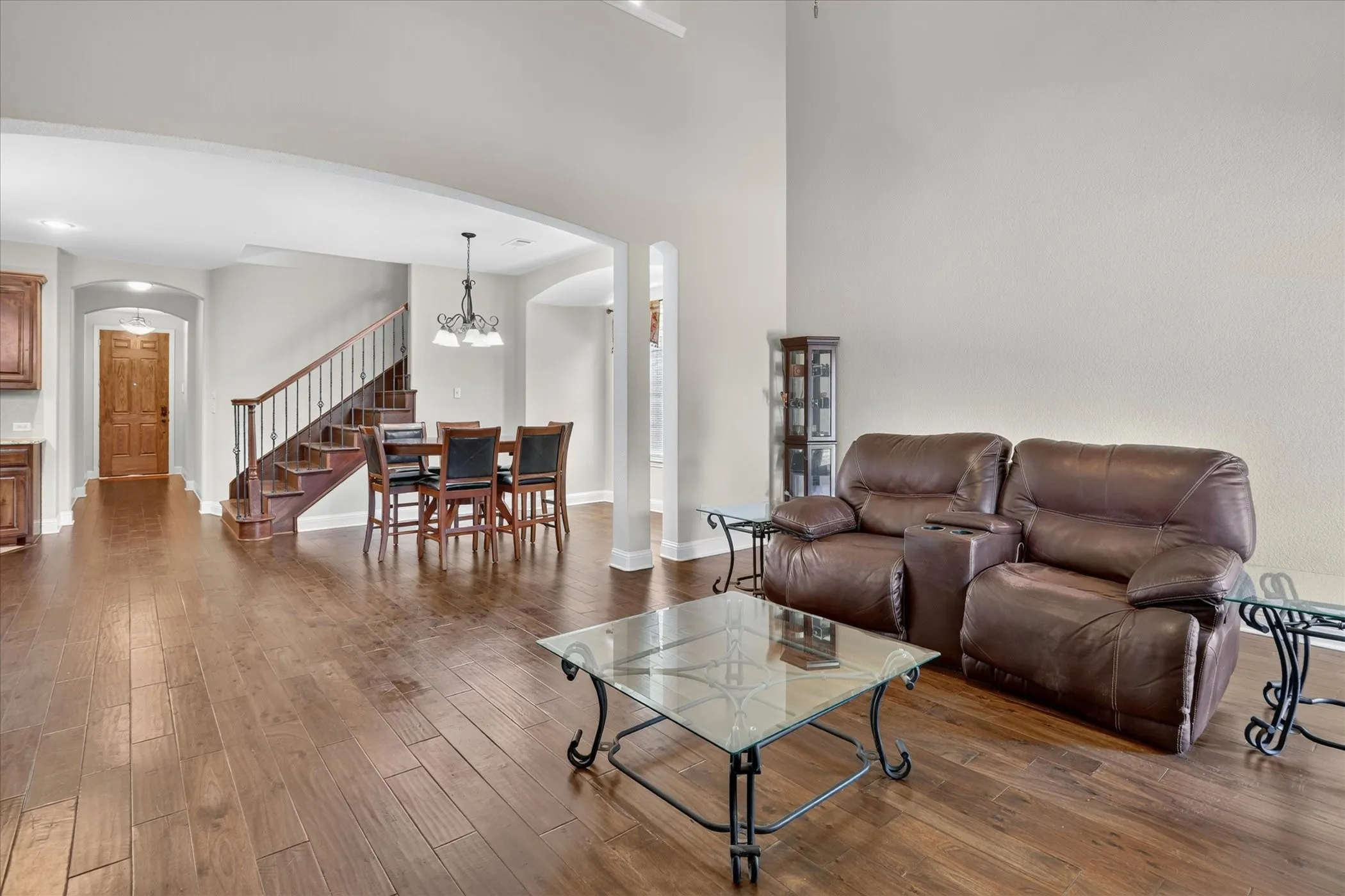 Spacious living area featuring wood-finish flooring, high ceilings, an elegant staircase with wood treads and a wrought iron banister, an arched entryway, and a formal dining area with a chandelier