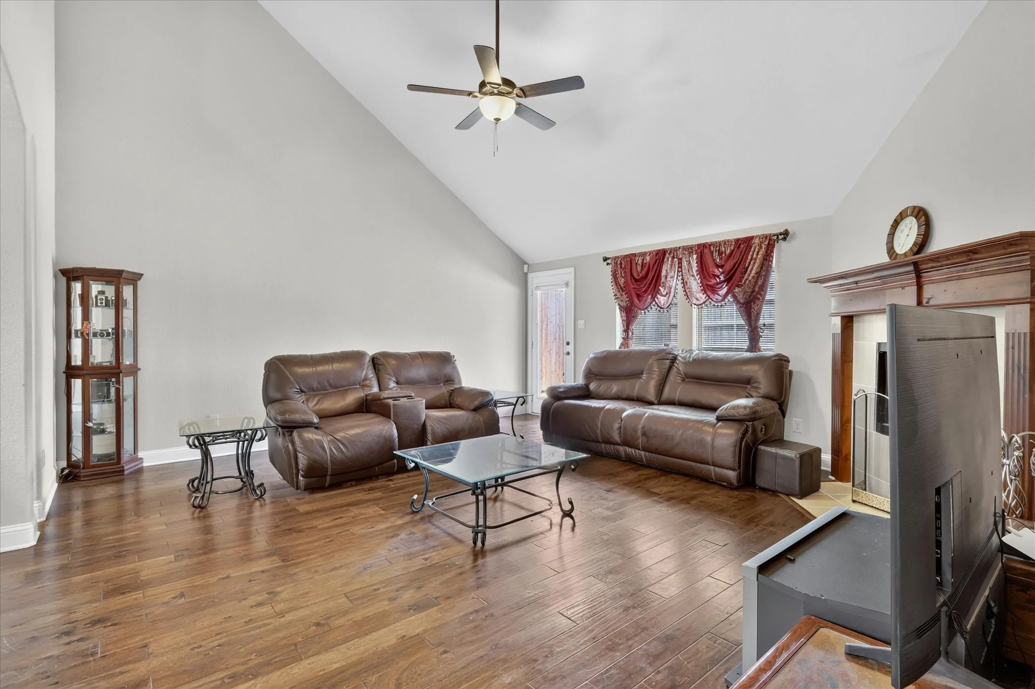 Living area featuring vaulted ceilings, wood-finish flooring, a ceiling fan with integrated lighting, and a fireplace with a wood mantel