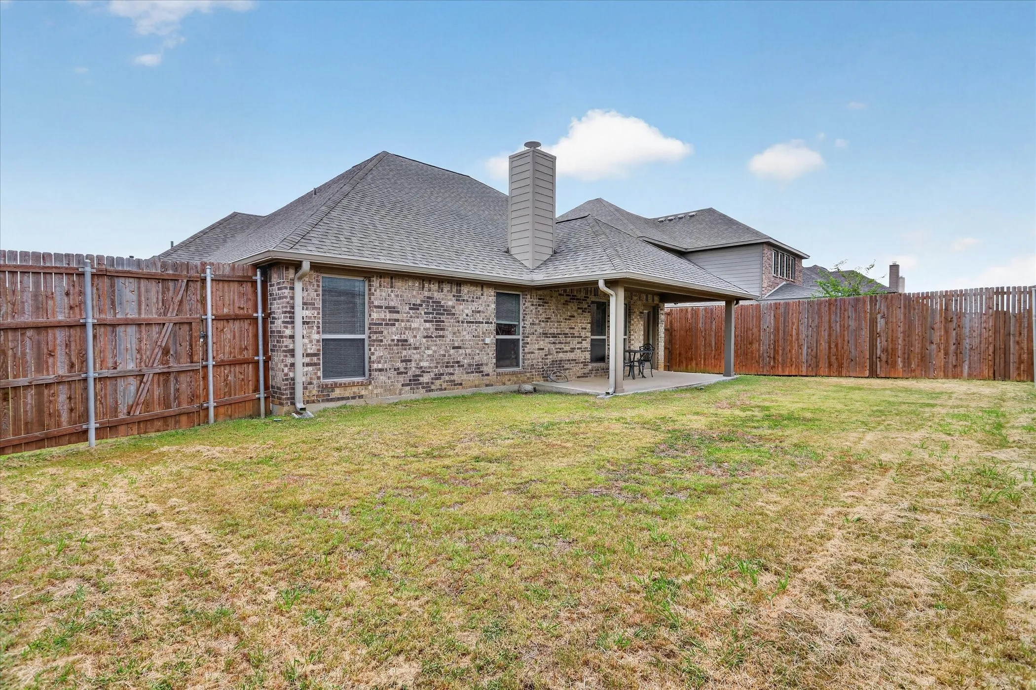 Expansive backyard featuring a brick exterior, covered patio, and a privacy fence
