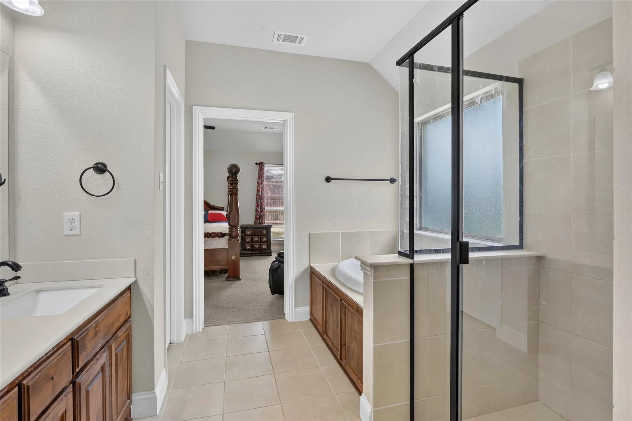 Bathroom featuring a walk-in shower with a frameless glass enclosure and black trim, a built-in tub with wood cabinetry, and a vanity with an undermount sink and light-toned countertop