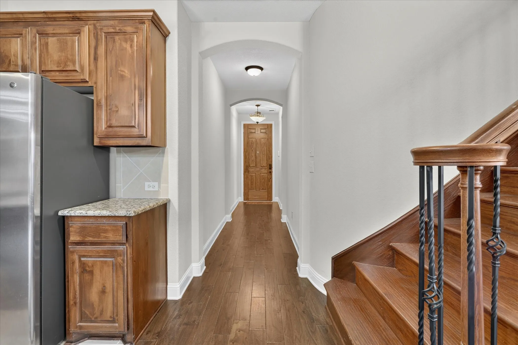 Hardwood flooring throughout a bright hallway with arched doorways, leading to a paneled wooden door