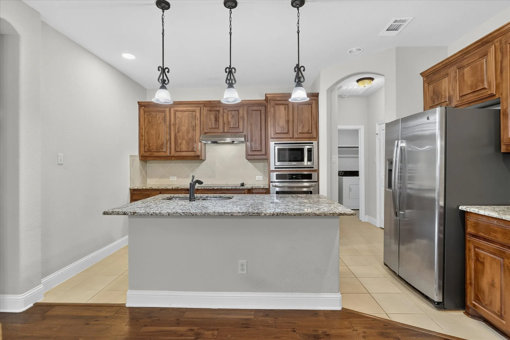 Kitchen island with granite countertop, integrated sink, and three pendant lights