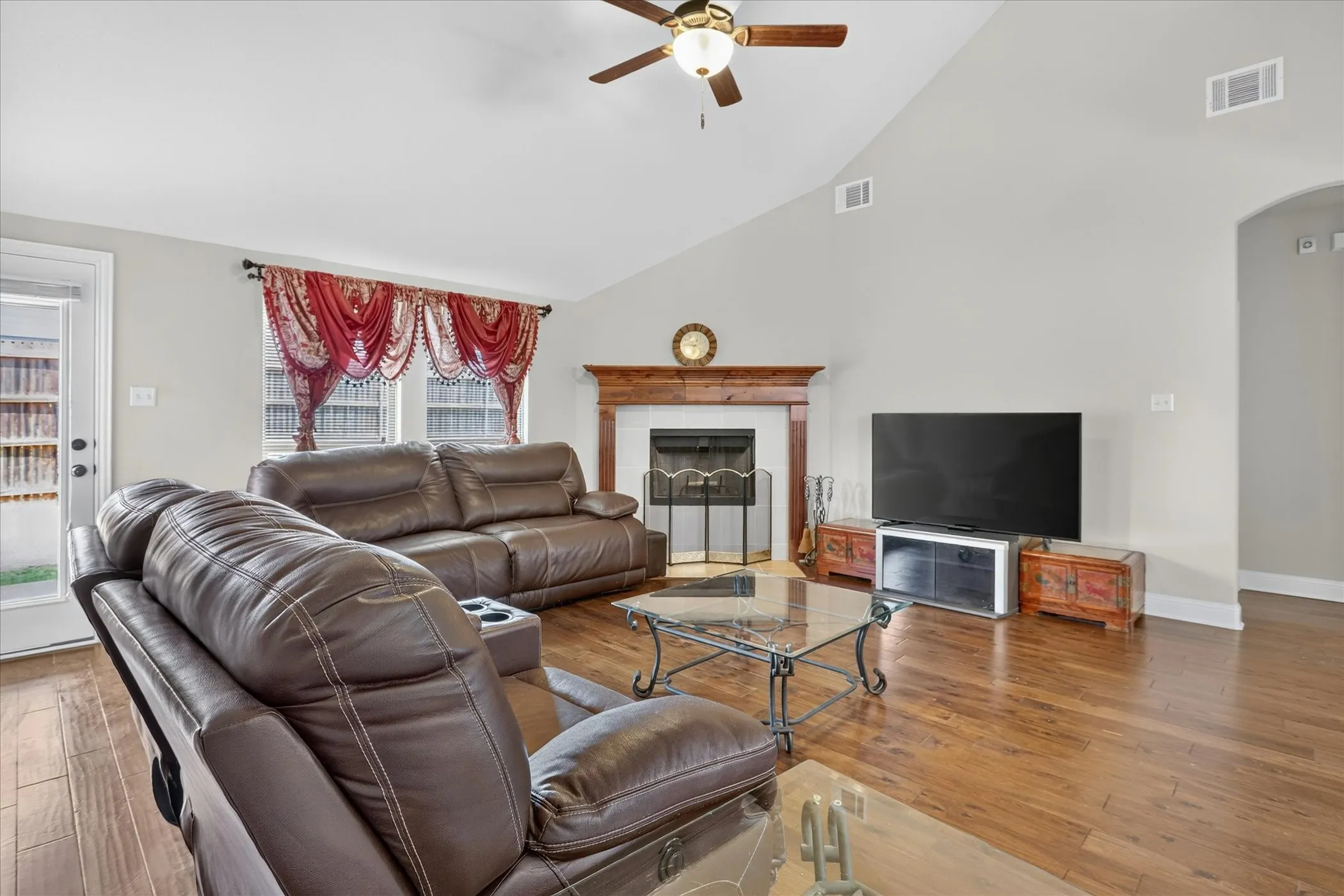 Living area featuring wood-finish flooring, a fireplace with a wood mantel, a vaulted ceiling, and an exterior door with glass panels