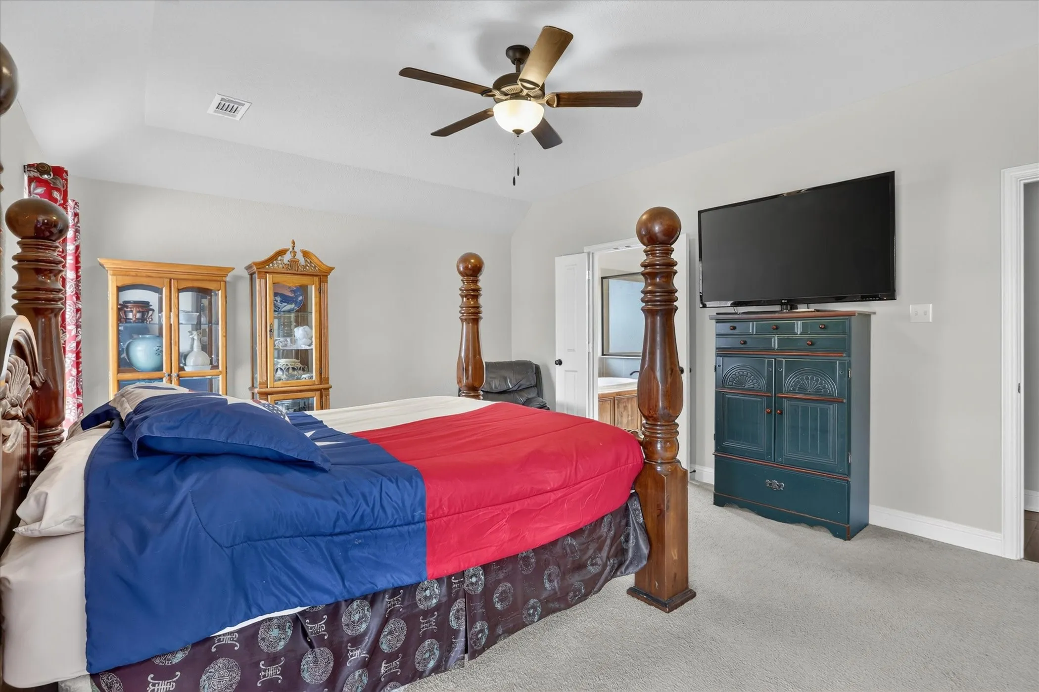 Carpeted bedroom with a ceiling fan light fixture and a door opening to a bathroom