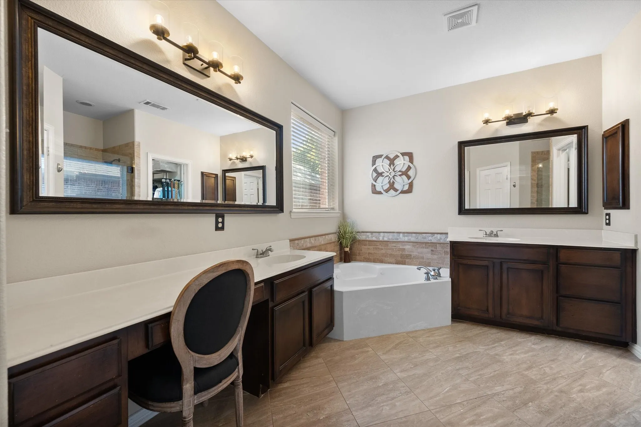 Spacious bathroom featuring a built-in vanity with dual sinks, an expansive mirror, and a corner soaking tub!