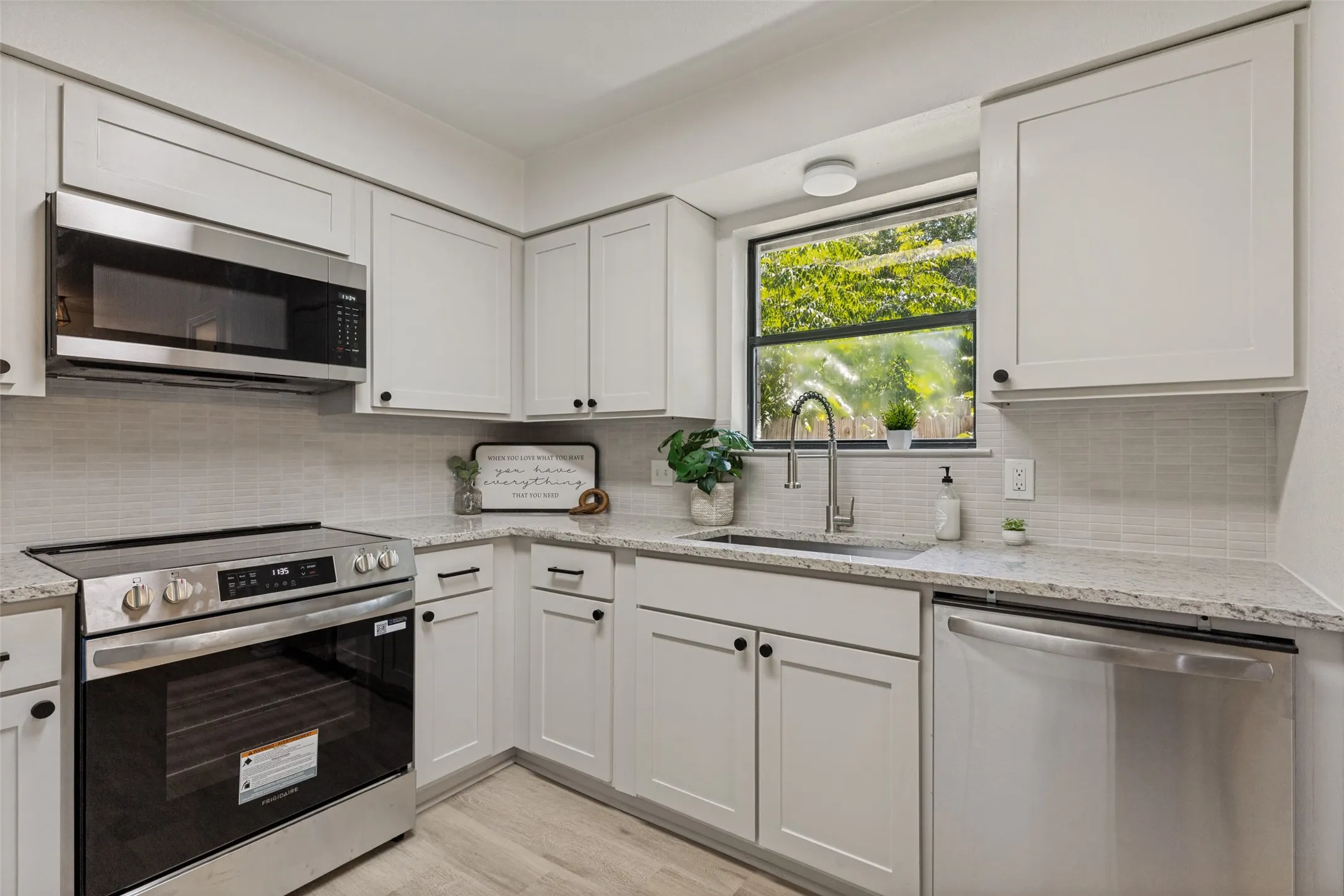 Kitchen featuring white shaker-style cabinetry, granite countertops, stainless steel appliances, and a light-toned tile backsplash