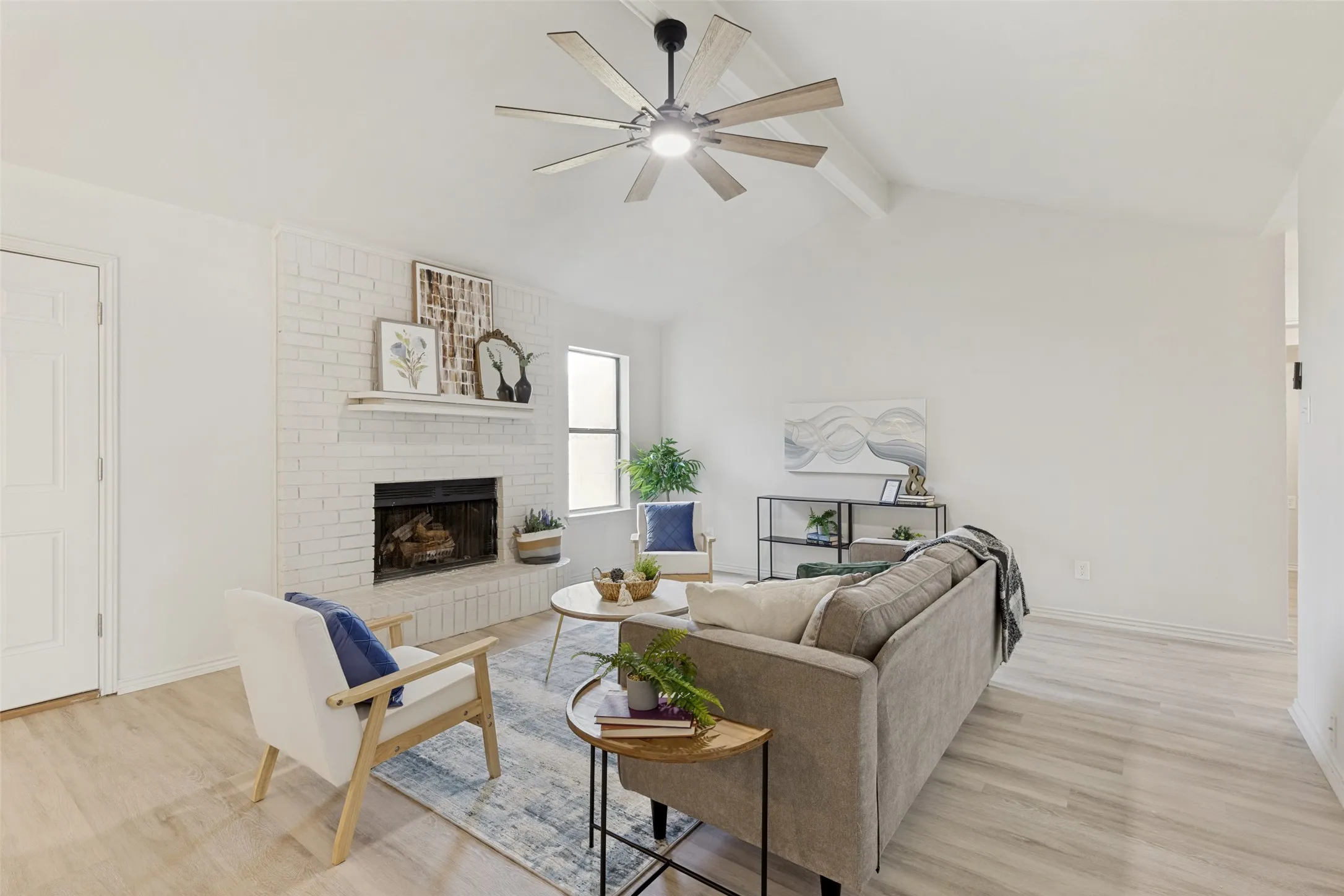 Living space featuring vaulted ceilings with exposed beams, wood-finish flooring, a white brick fireplace with a mantle, and a ceiling fan