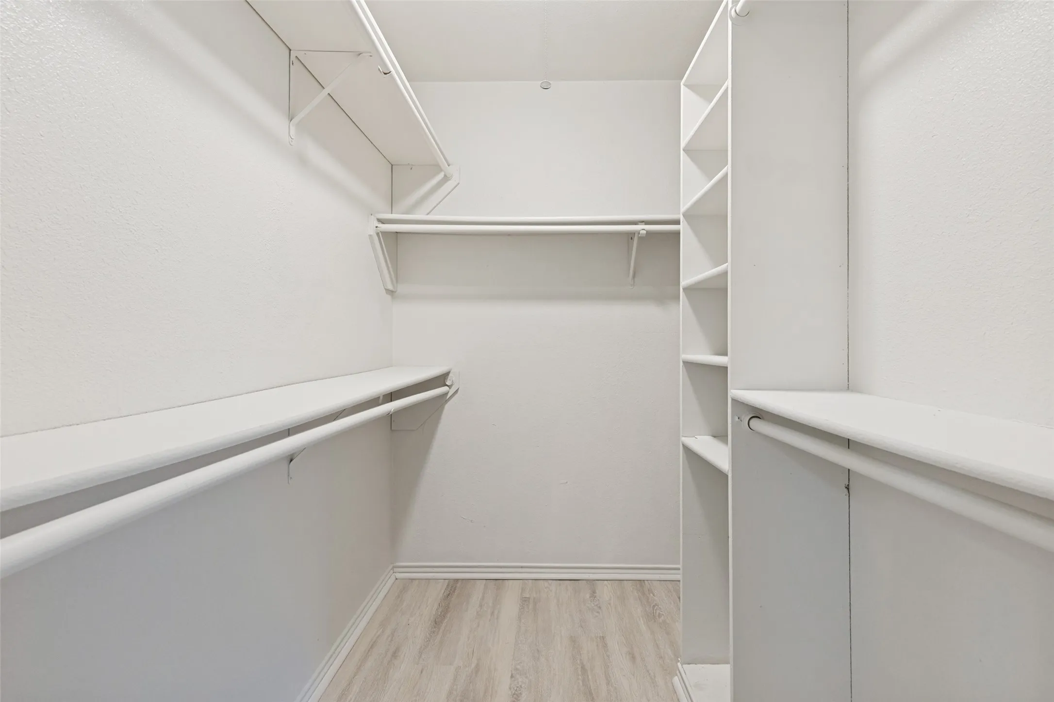 Walk-in closet featuring white wire shelving, hanging rods, built-in vertical shelving, and wood-finish flooring