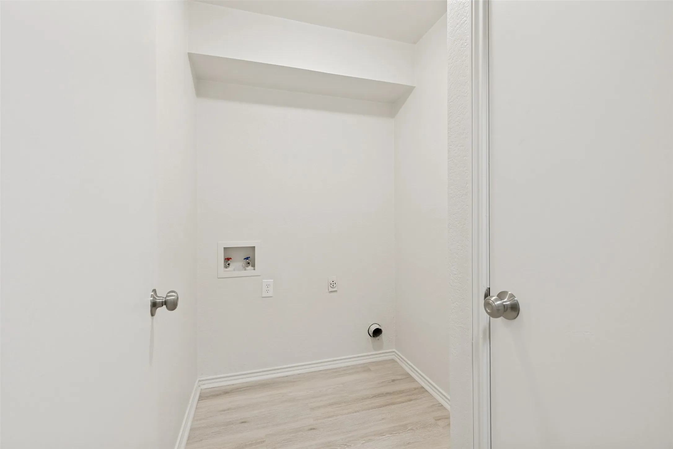 Dedicated laundry area featuring light wood-finish flooring, white baseboards, and a recessed utility box with hookups