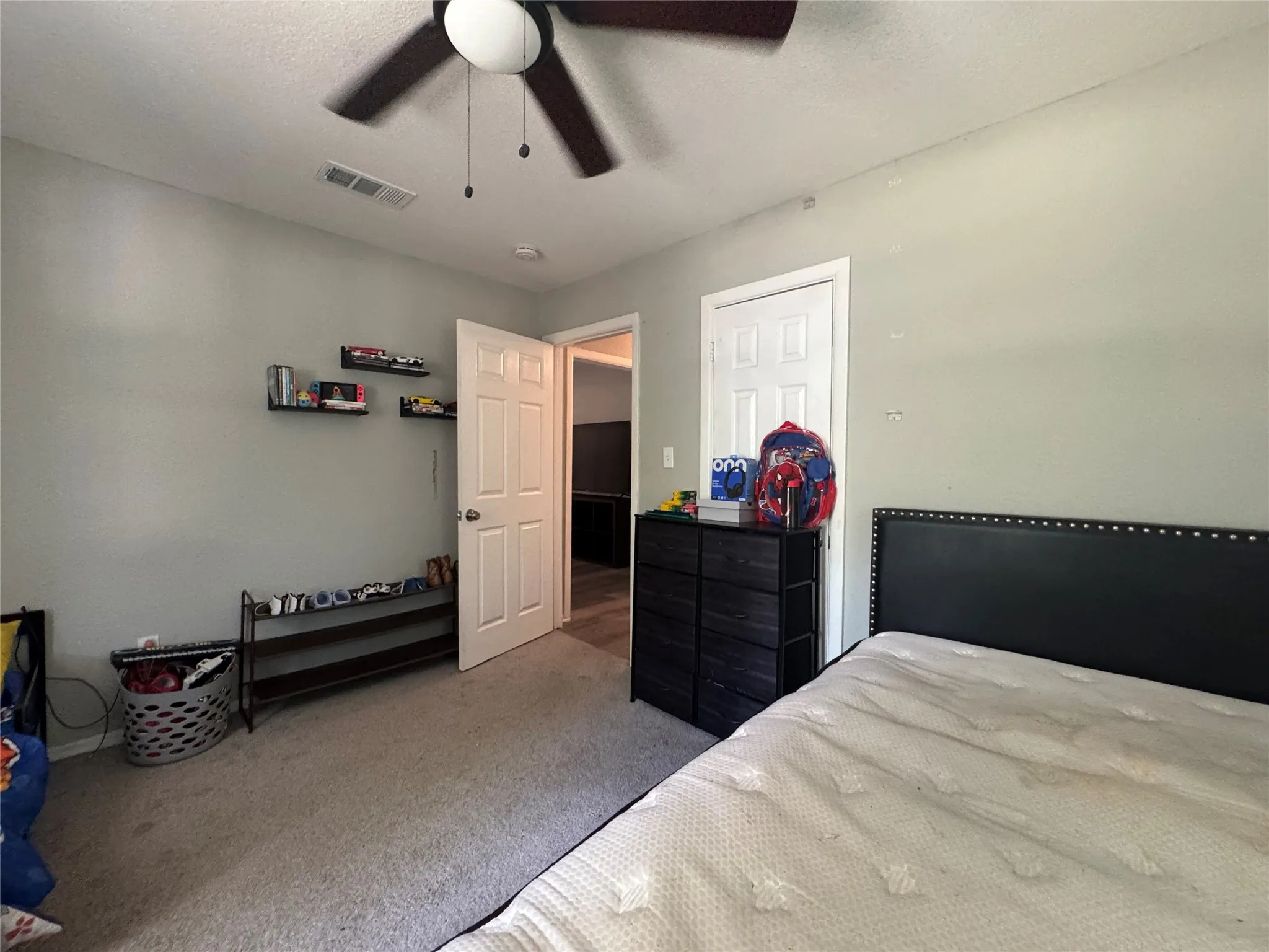 Carpeted room featuring a ceiling fan with light, light grey painted walls, a white paneled door, and three wall-mounted shelves