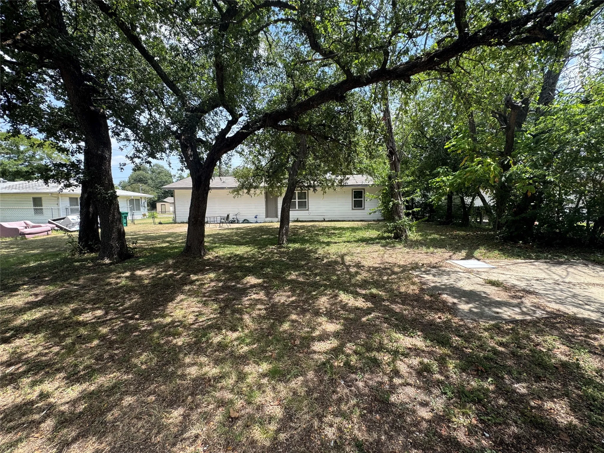 Front yard featuring mature trees and a white-sided residence with multiple windows