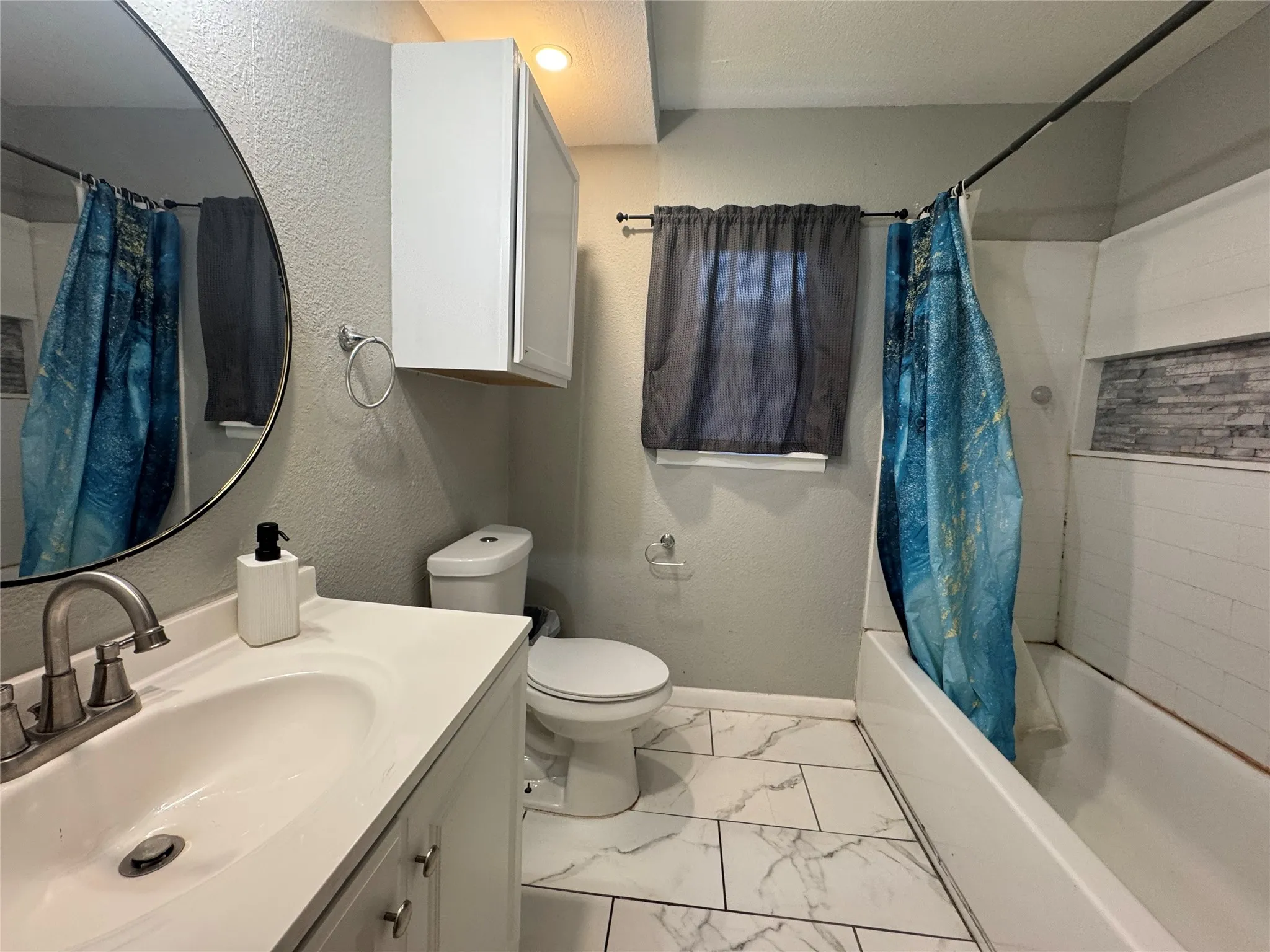 Bathroom featuring a white vanity with an integrated sink, brushed nickel faucet, a round wall mirror, and modern tile flooring