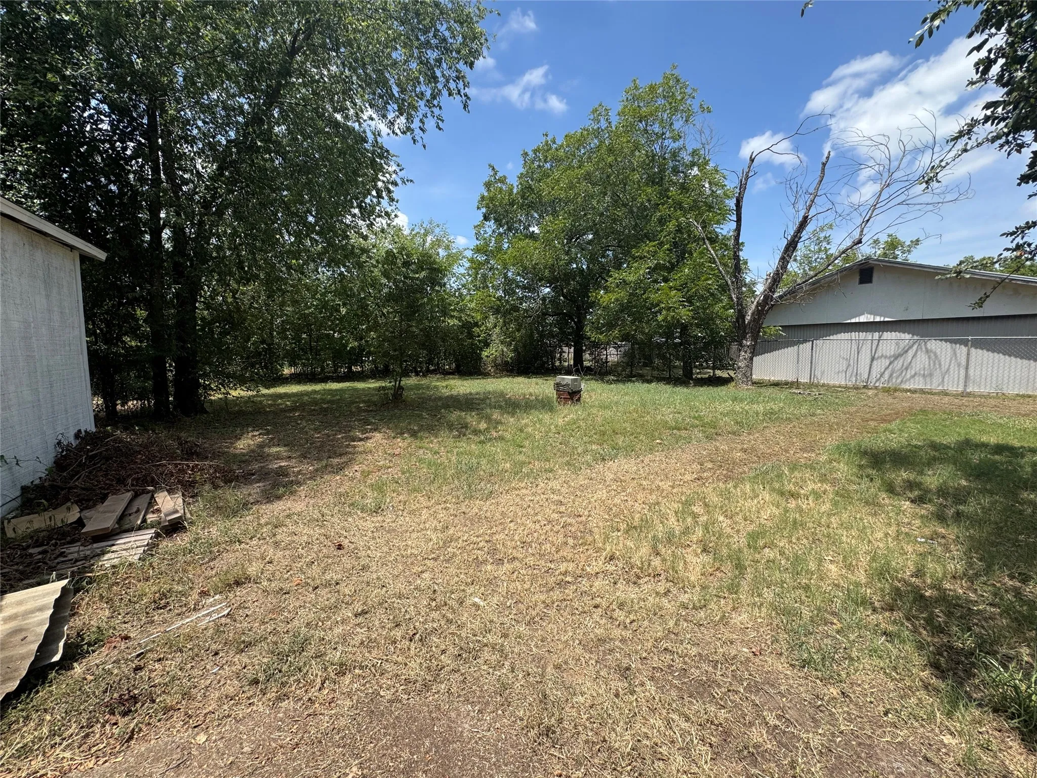 Expansive outdoor space featuring mature trees, partial fencing, and a separate structure with siding