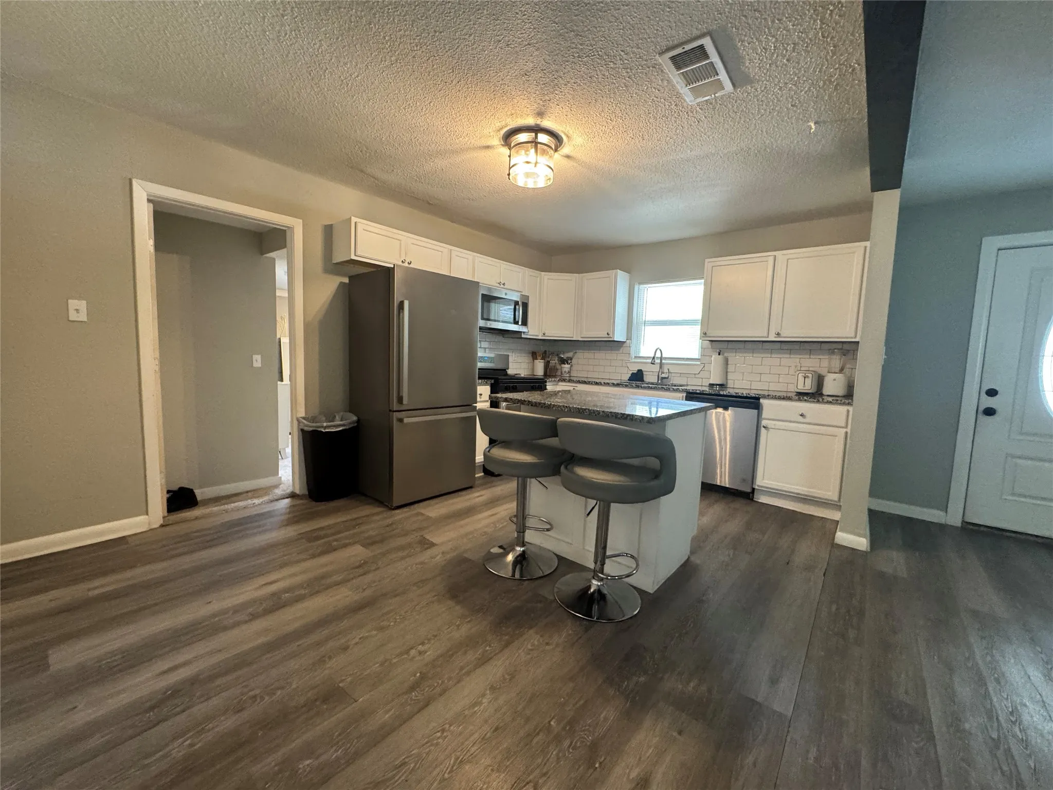 Contemporary kitchen featuring white cabinetry, stainless steel appliances, a white subway tile backsplash, and an island with a stone-finish countertop