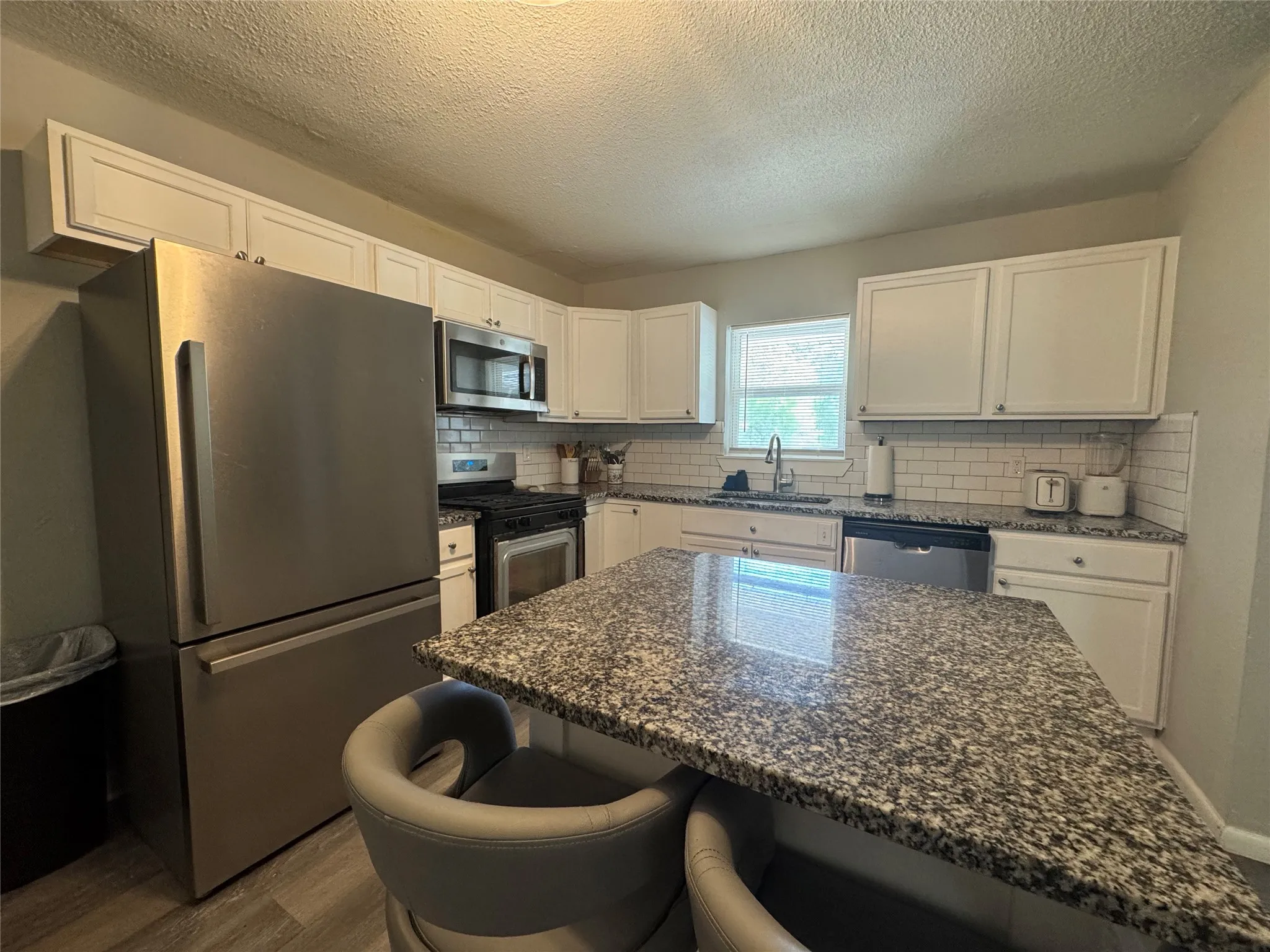 Kitchen featuring a central island with a speckled countertop, white cabinetry, stainless steel appliances, and a subway tile backsplash
