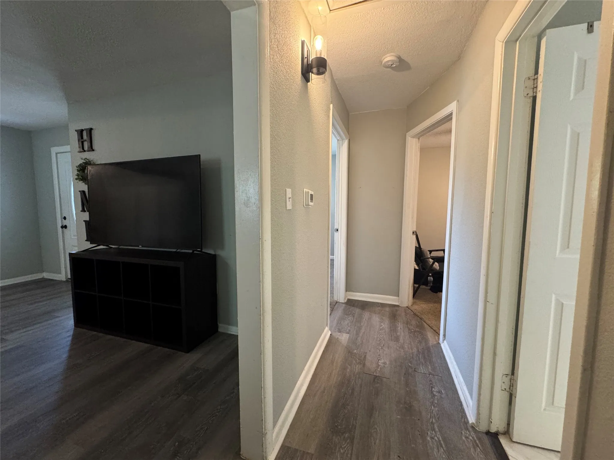 Hallway featuring wood-finish flooring, light grey walls, white trim, and a modern wall sconce