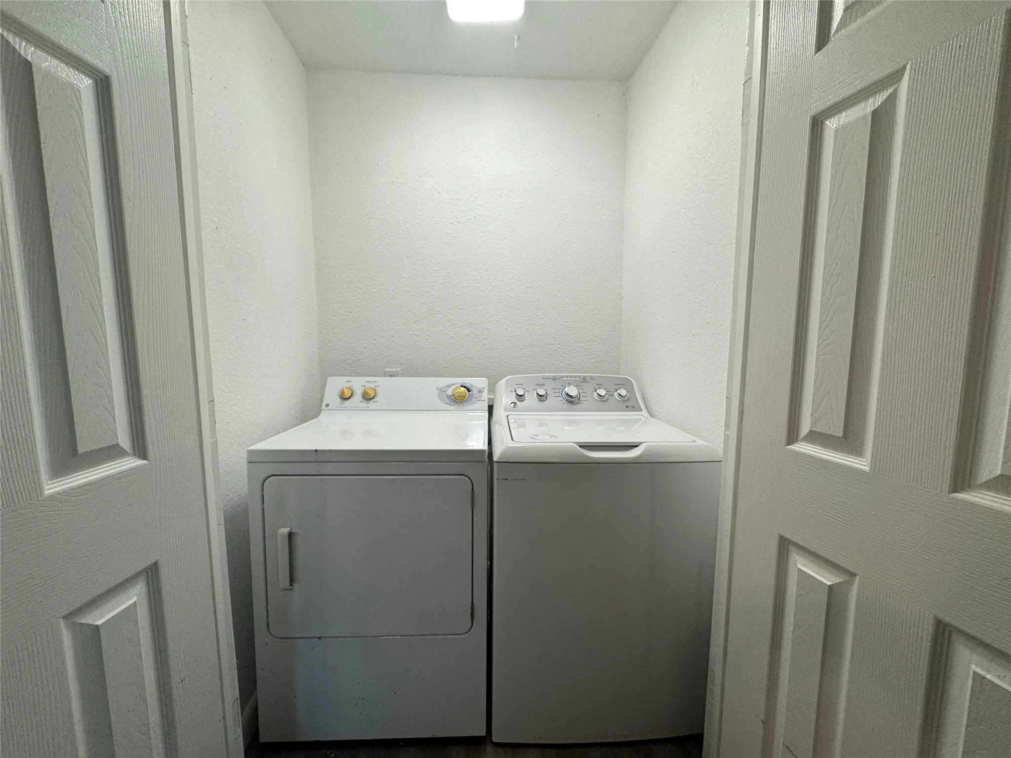 Dedicated laundry area with textured white walls, a built-in overhead light fixture, and wood-finish flooring