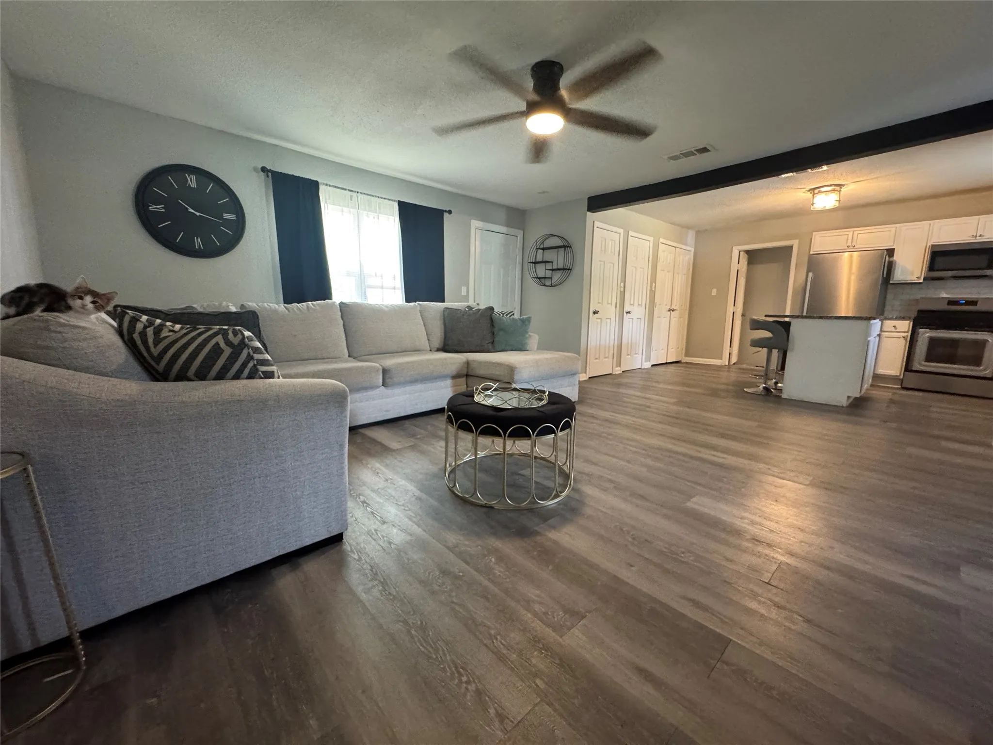 Spacious living area featuring wood-finish flooring, a ceiling fan, and ample natural light from multiple windows